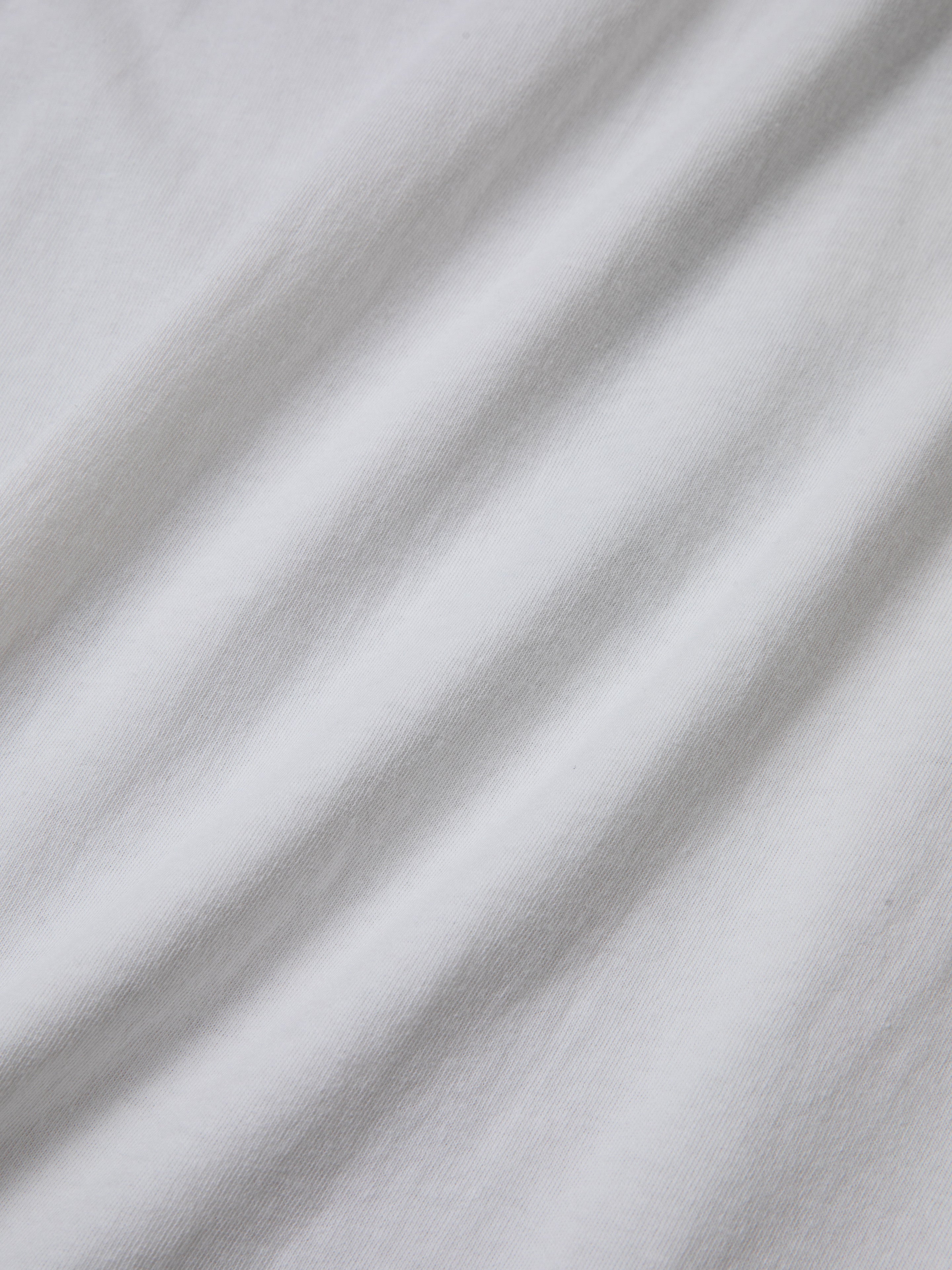 A close-up view of the white, slightly wrinkled fabric surface of the Sunflower Tee by FOUND, showcasing a hint of a floral graphic that exudes a vintage feel.