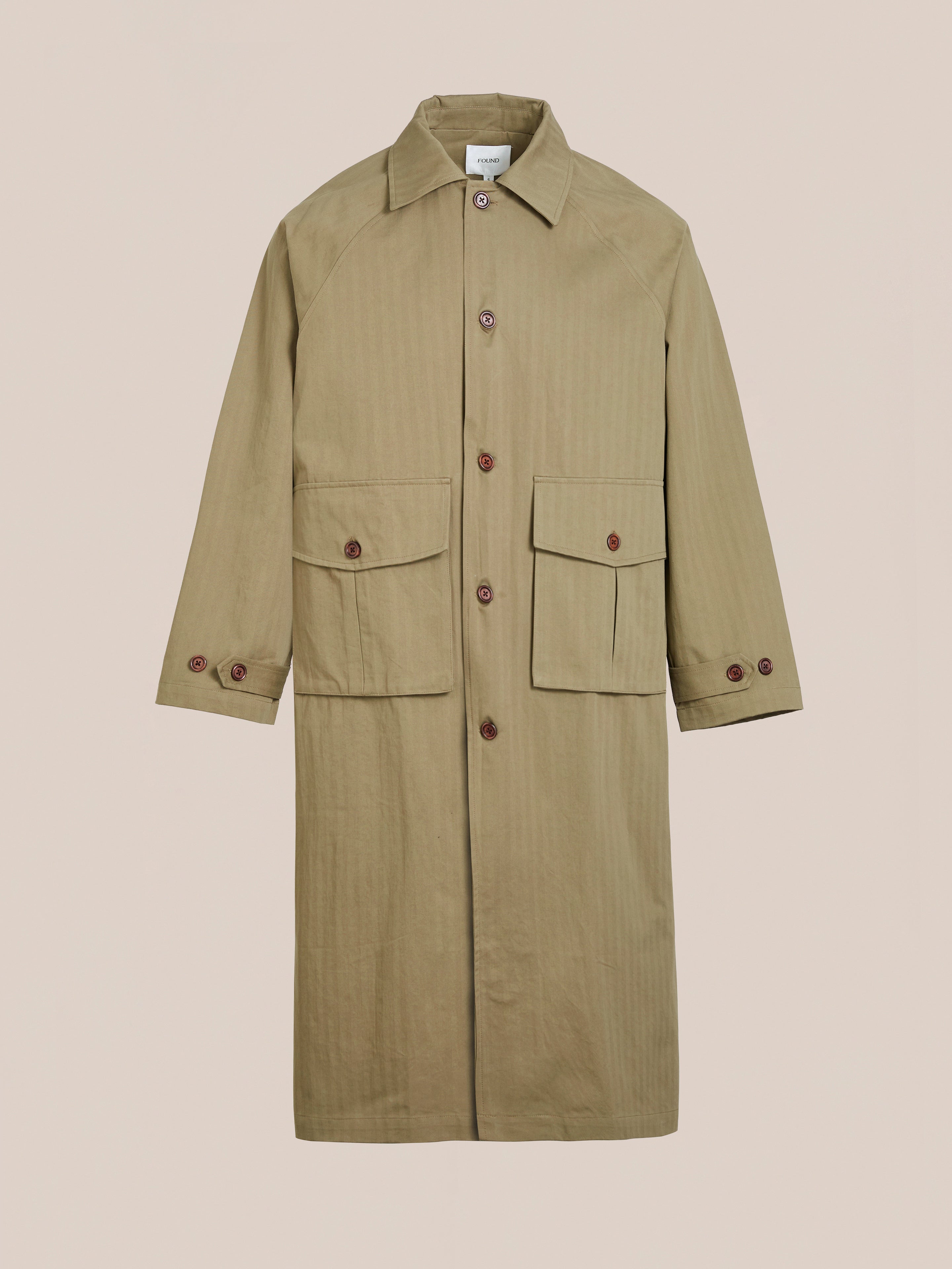 Tan Herringbone Twill Trench Coat by FOUND with a relaxed fit, utility pockets, and buttoned cuffs. Displayed on a plain background.