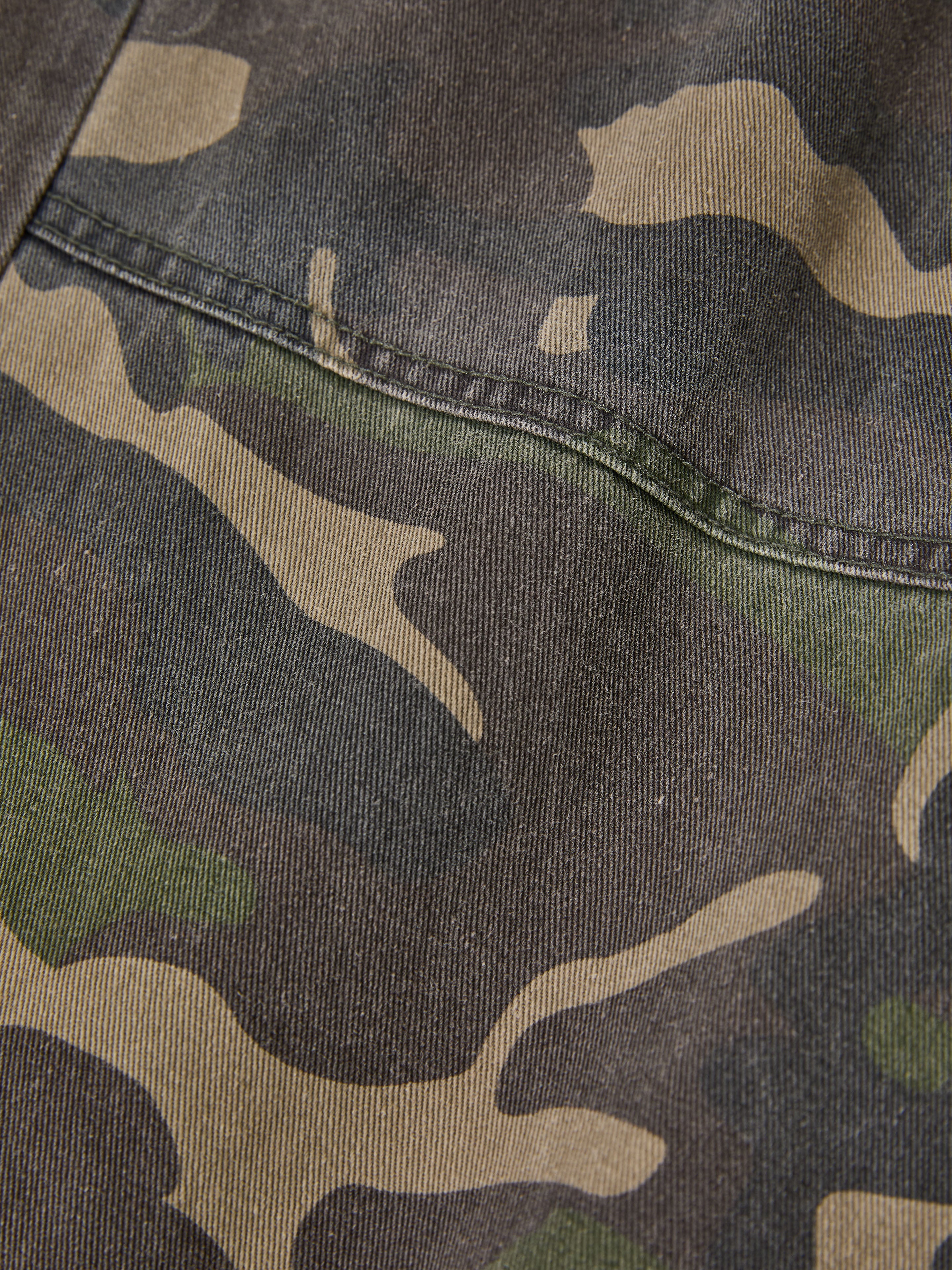 A close-up of the fabric shows the green camouflage pattern and visible seam, reflecting the vintage style of FOUND's Camouflage Twill Utility Cargo Pants.