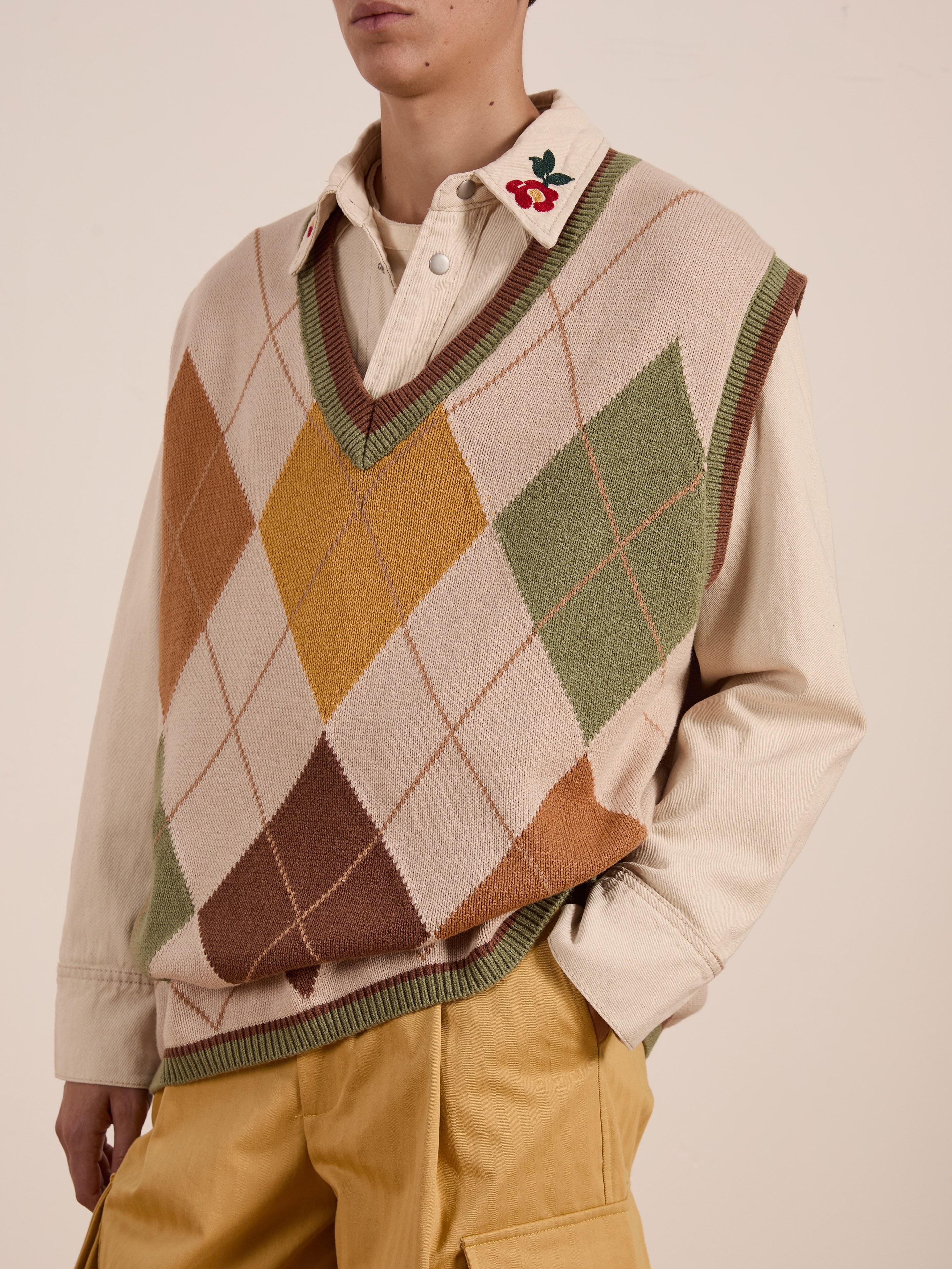 Person wearing a beige shirt with a floral collar, FOUND's Argyle Knit Vest with a vintage diamond pattern, and unisex relaxed-fit mustard pants.