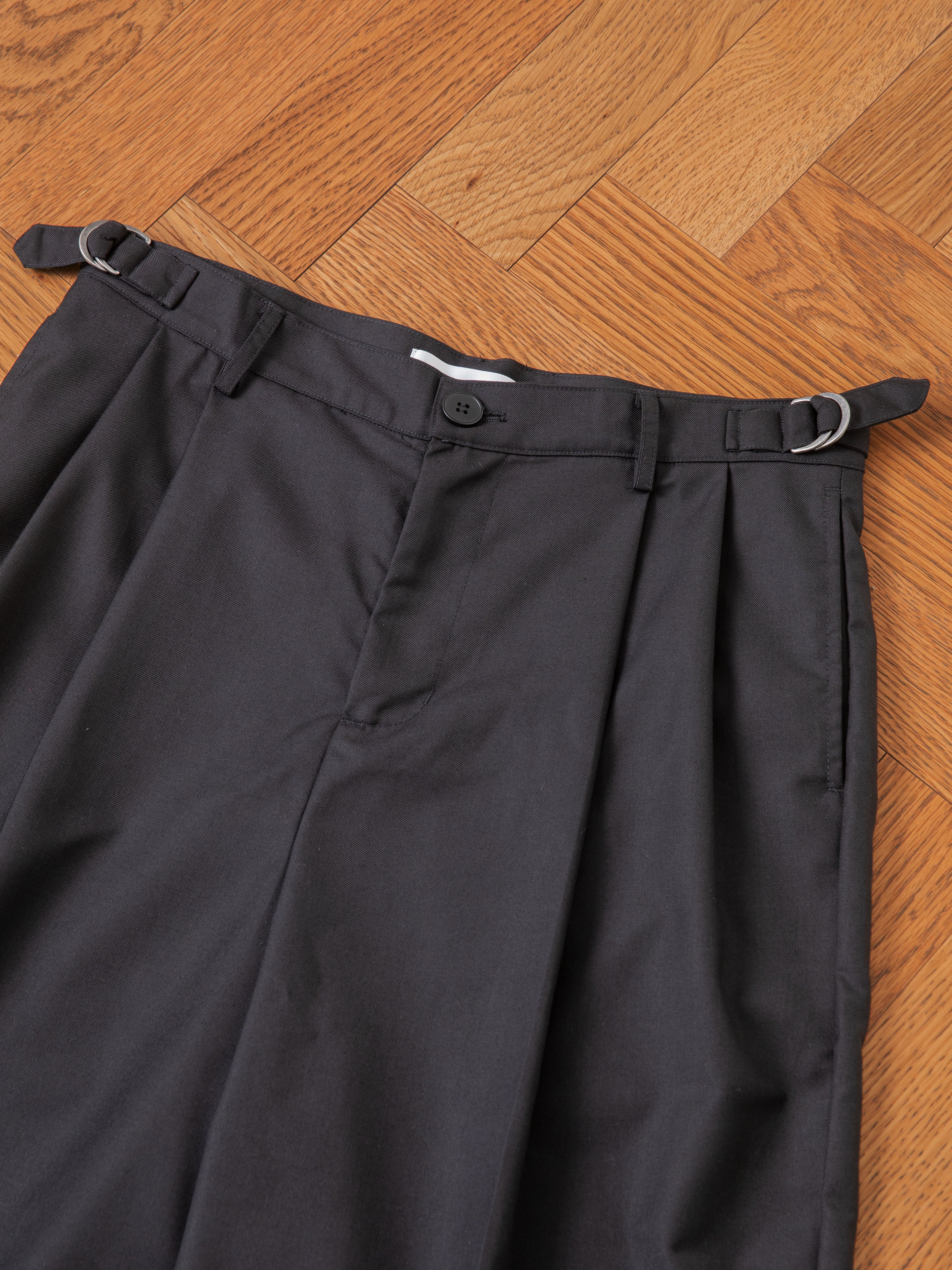 FOUND Pleated Trouser Shorts in navy blue, featuring double pleats, an adjustable waist, belt loops, and a button closure, are laid flat on a wooden floor.