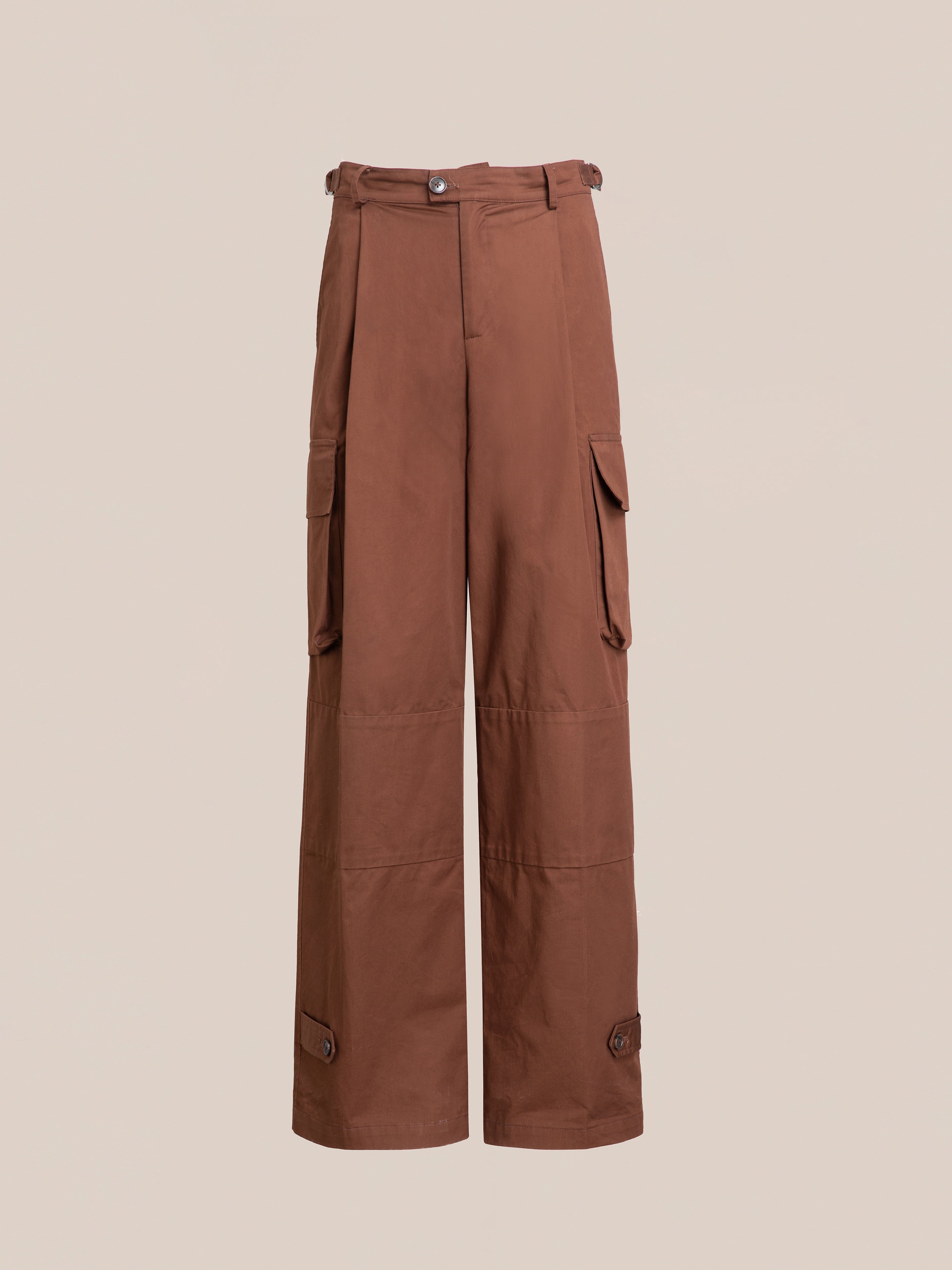 FOUND's Pleated Pocket Trousers in brown feature side cargo pockets, a button and zip closure, and adjustable ankle straps, all showcased against a plain background.