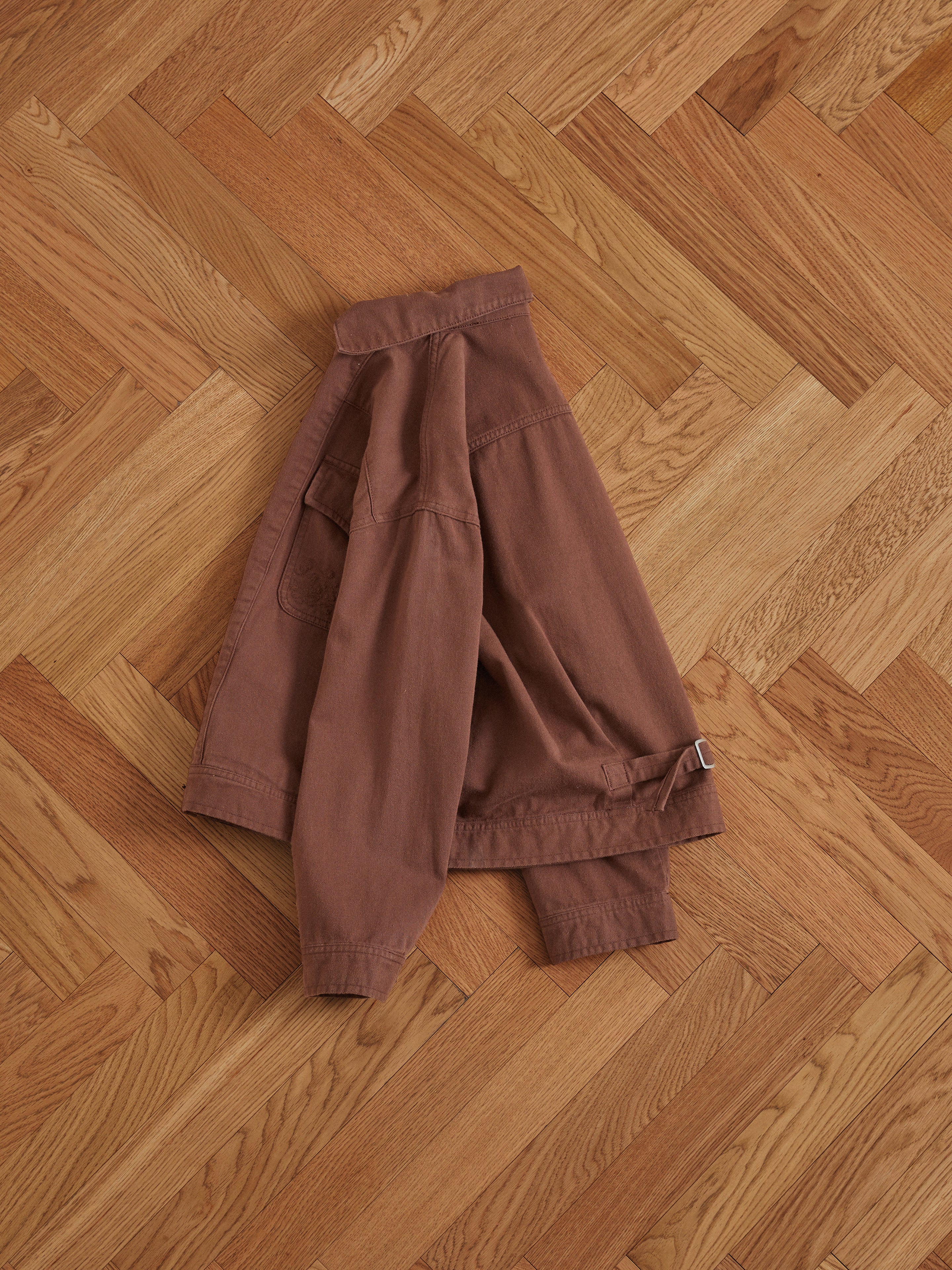 A Dusky Western Trucker Jacket with antique blue stone buttons is laying on a wooden floor.