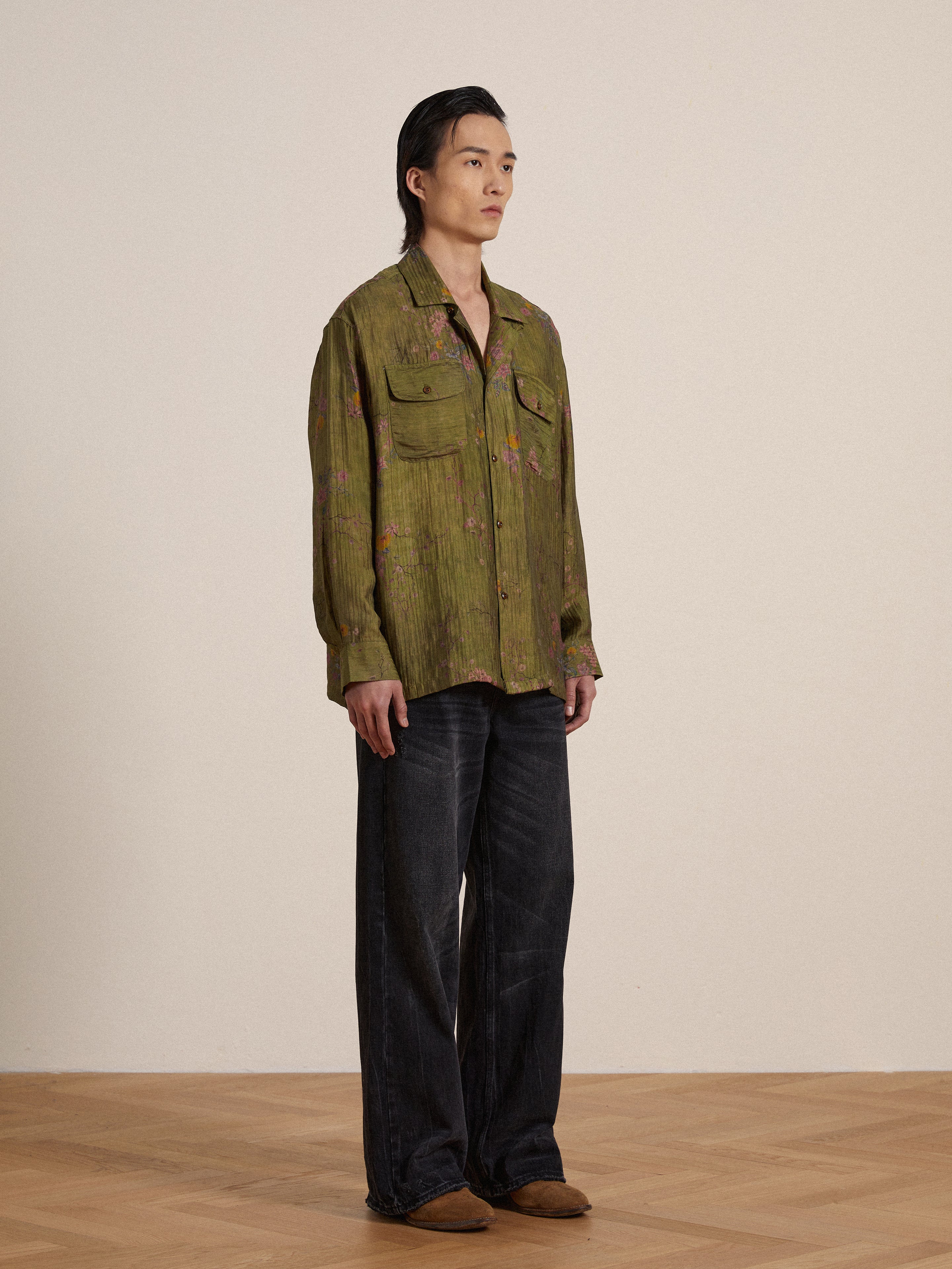 A man in a Found Floral Moss LS Camp Shirt standing on a wooden floor.