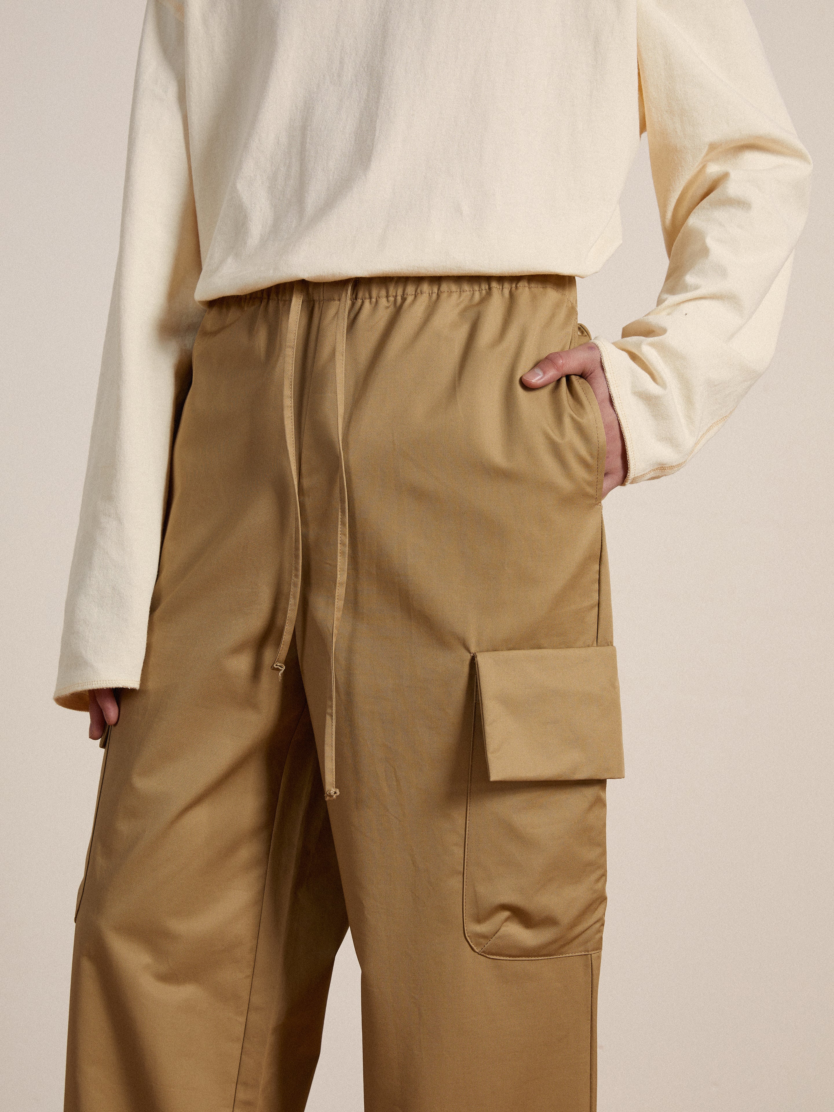 A man wearing Found Twill Cargo Drawstring Pants in tan.