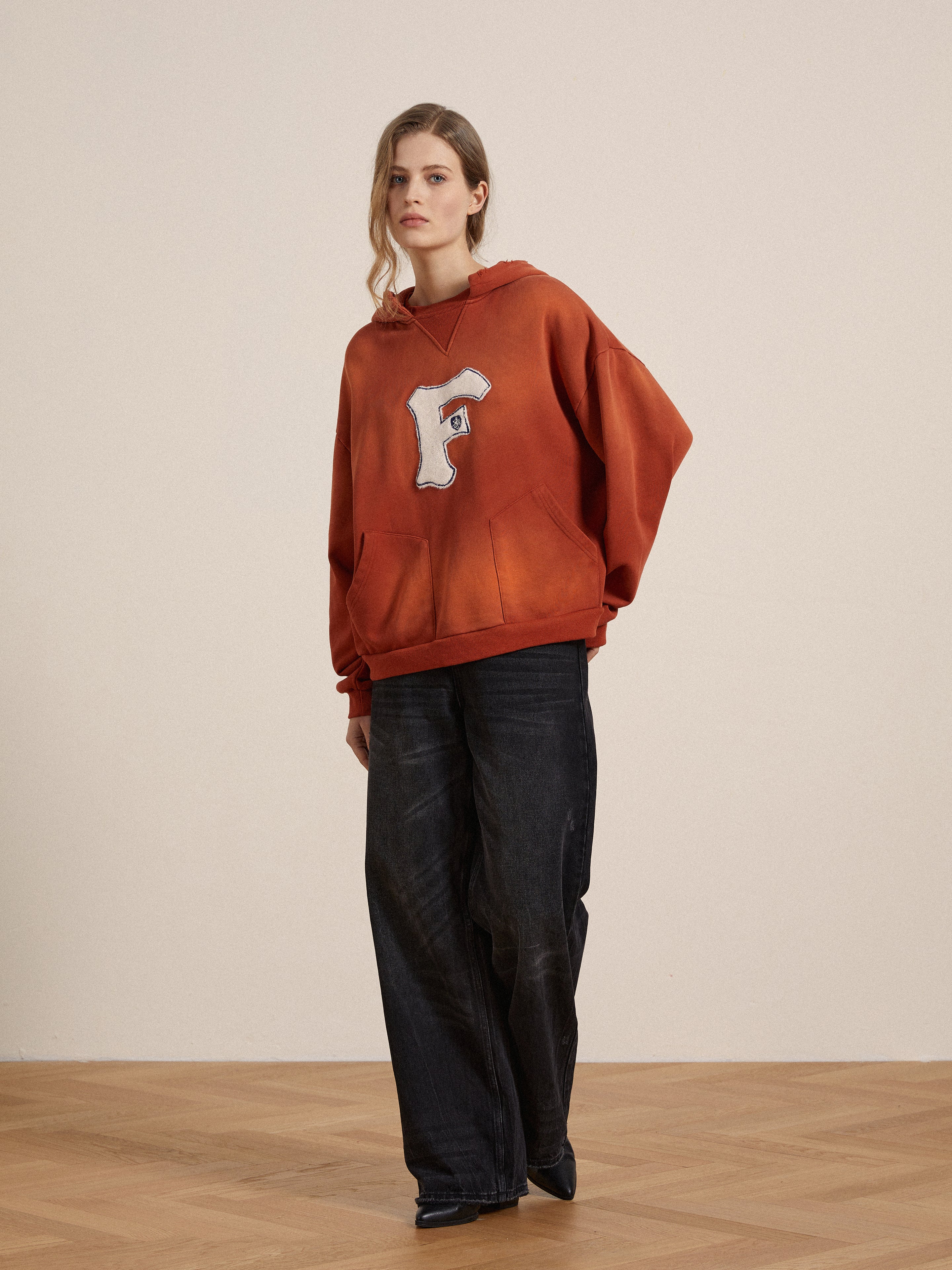 A woman wearing a Found faded "F" hoodie in enzyme washed cotton and black pants.