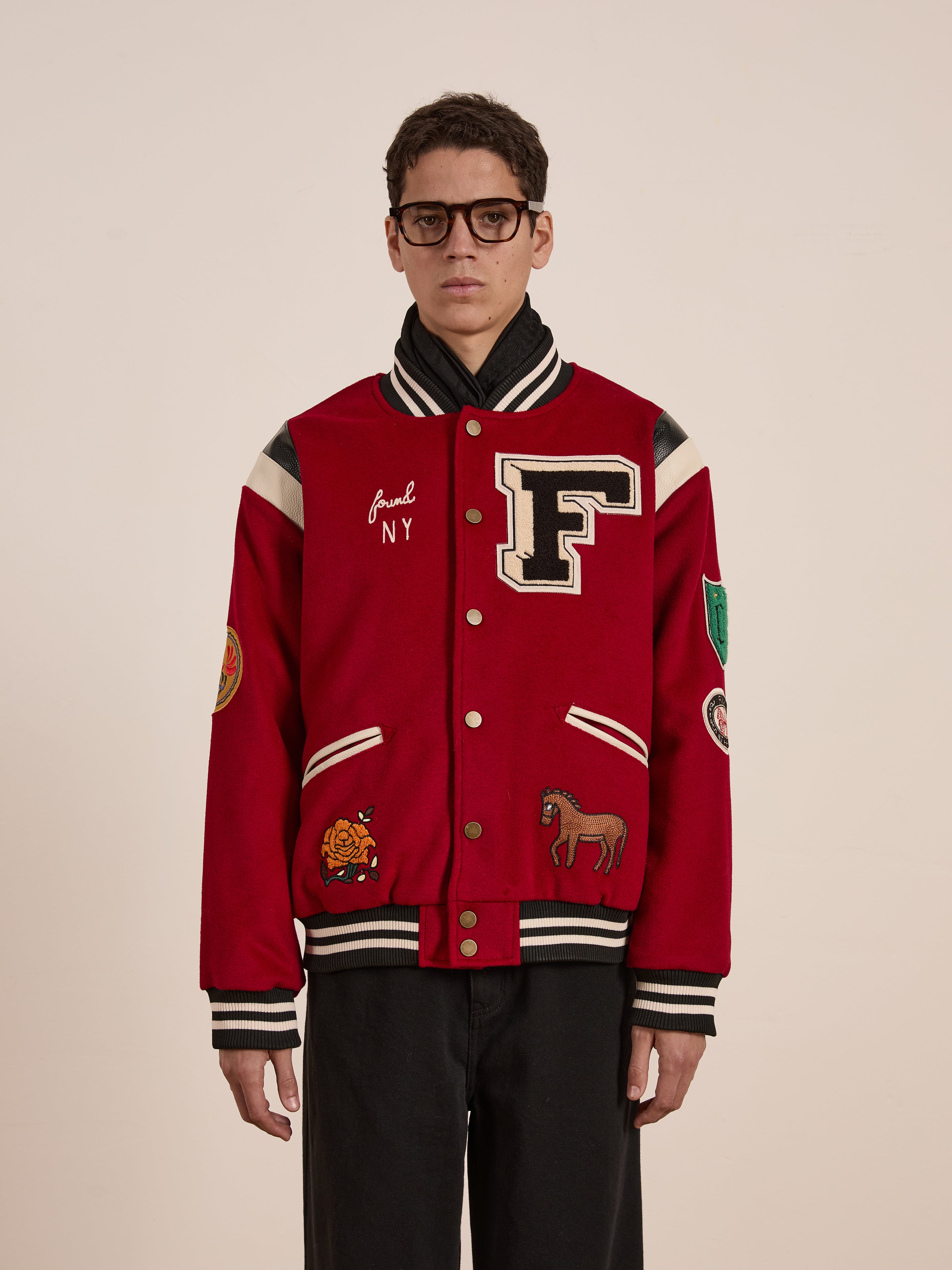 A person in a red FOUND Letterman Varsity Jacket with a chenille chest logo and patches, including a large "F," stands against a plain background.