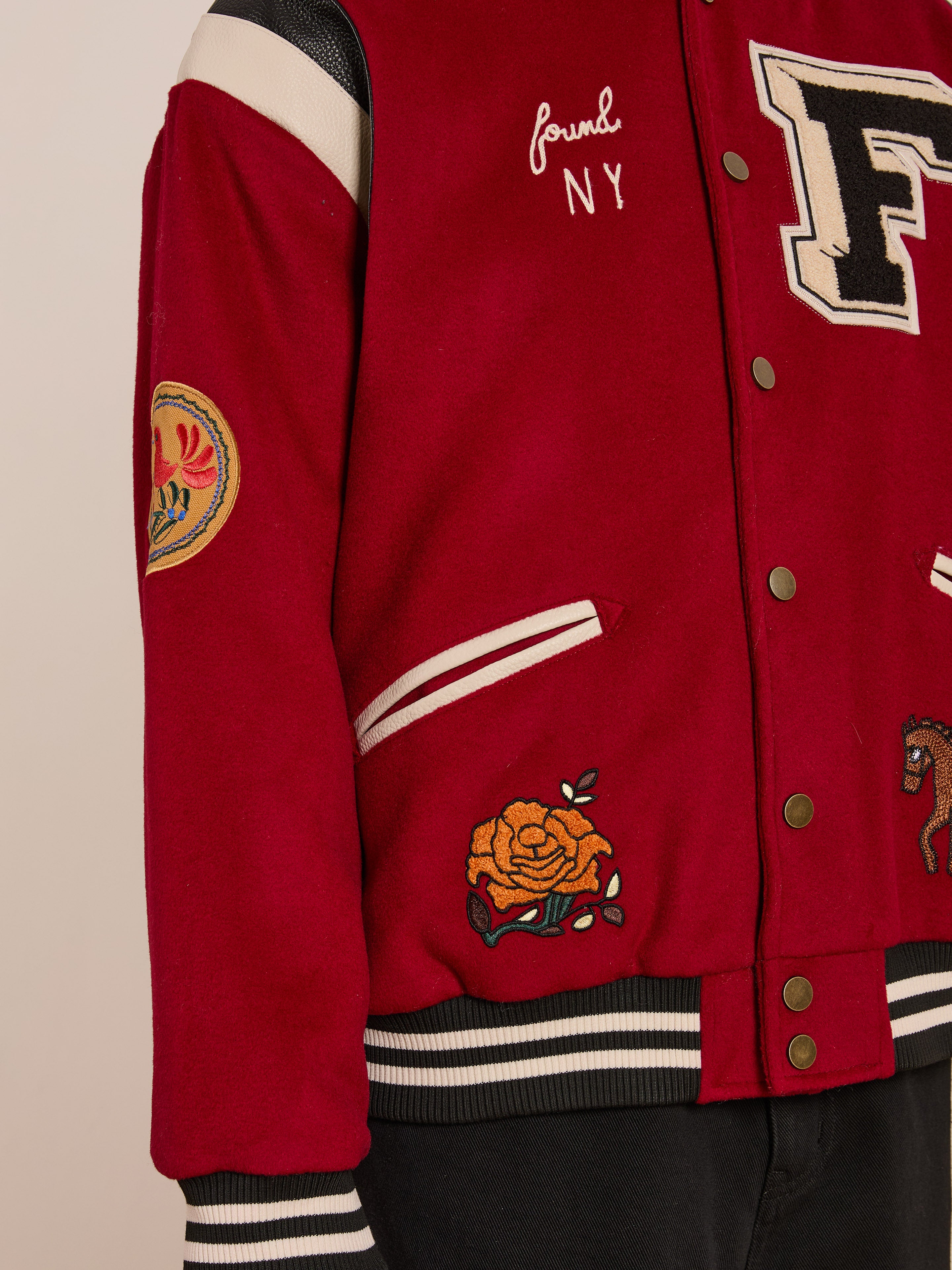 A close-up shows someone in a FOUND Letterman Varsity Jacket, unisex with a relaxed fit. It features patches like a large "F," rose, "NY" text, and a unique chenille logo on the chest.