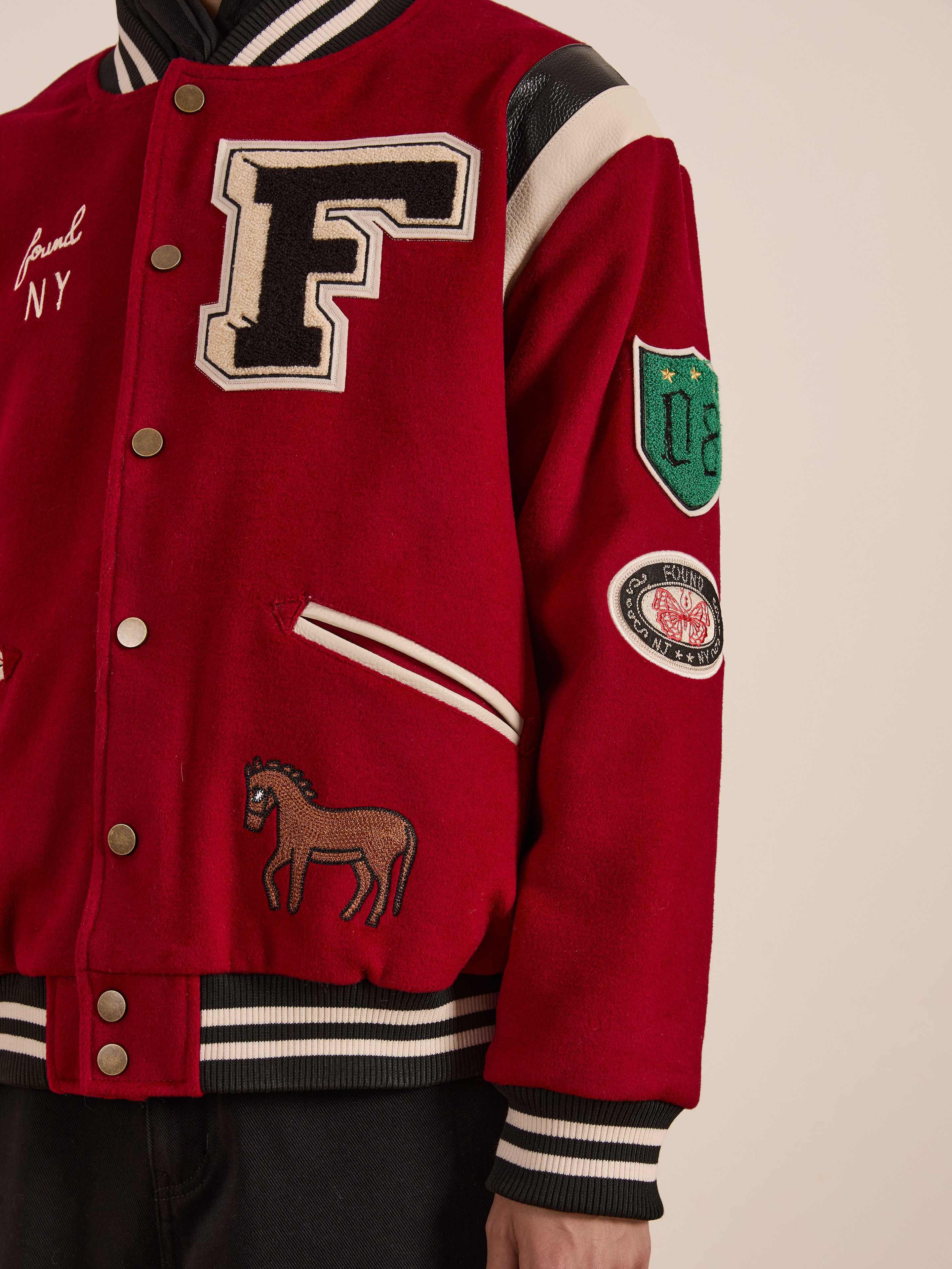 The FOUND Letterman Varsity Jacket has a relaxed fit with a vibrant red design that features patches, including a large chenille "F" logo on the chest and artistic horse emblems on the sleeves and chest.