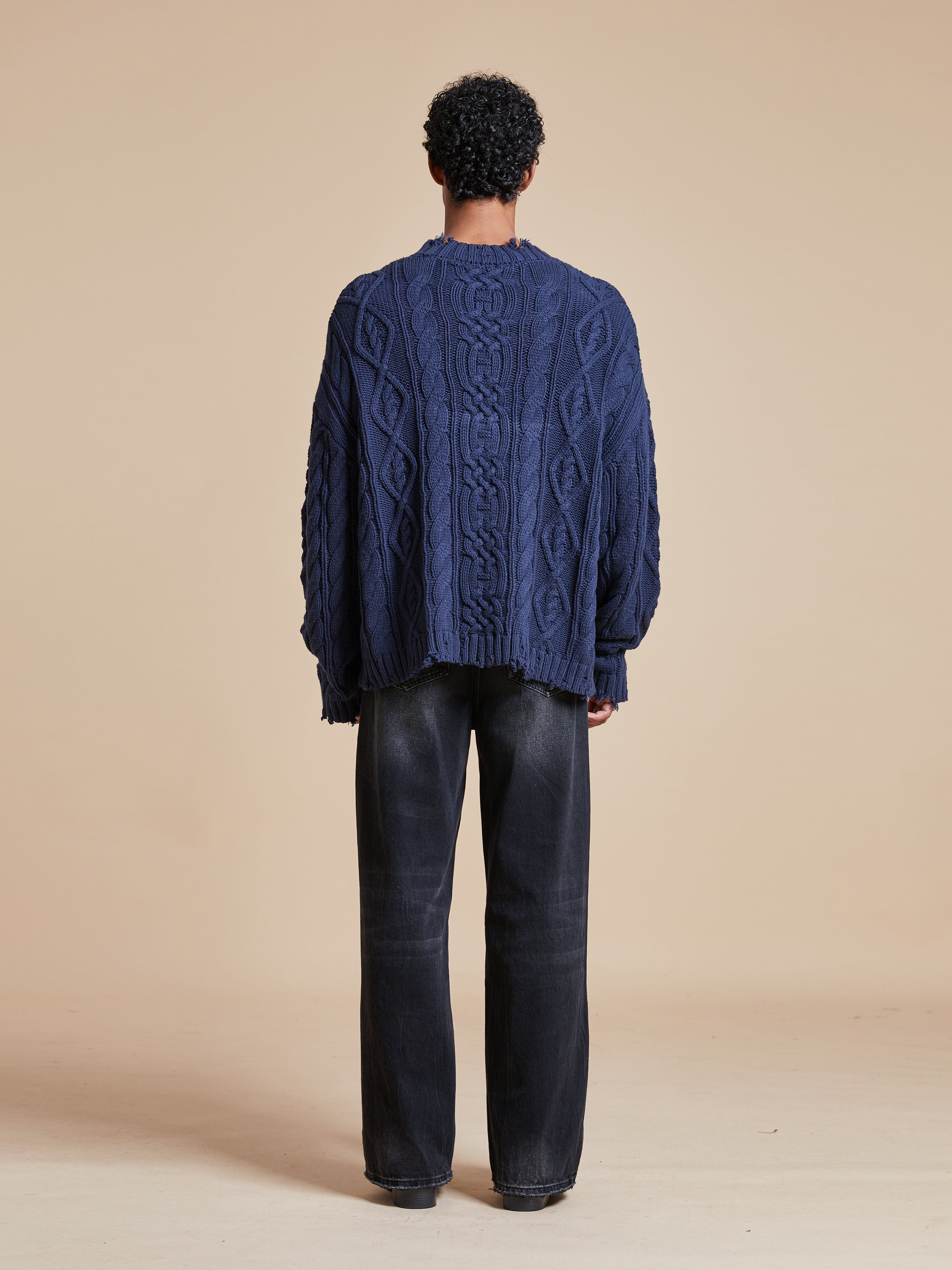 The back view of a man wearing an Astral Distressed Cable Knit Sweater made by Found.