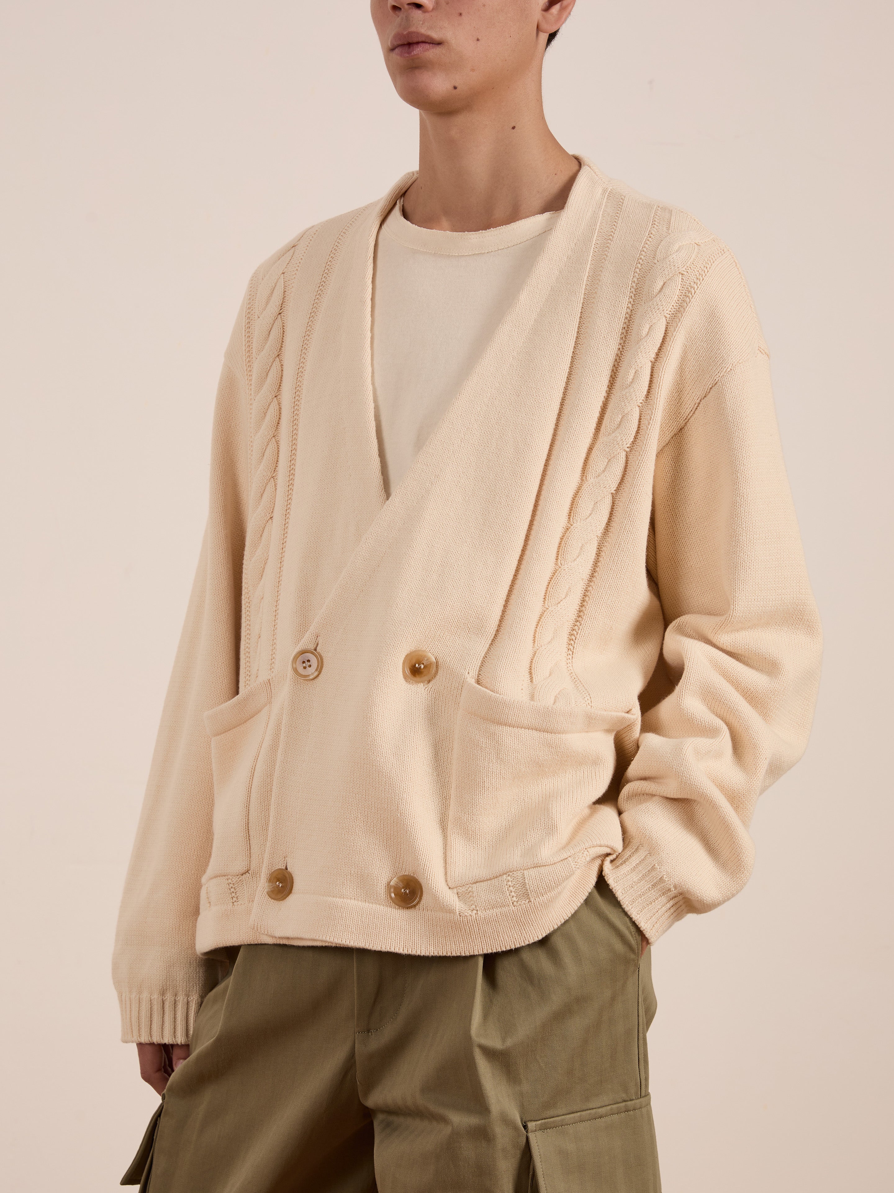 Styled in a chic cream-colored Double Breasted Knit Cardigan by FOUND, featuring braided details and large pockets, this outfit combines a midweight cotton blend with a white top and relaxed olive green pants for an effortlessly stylish look.