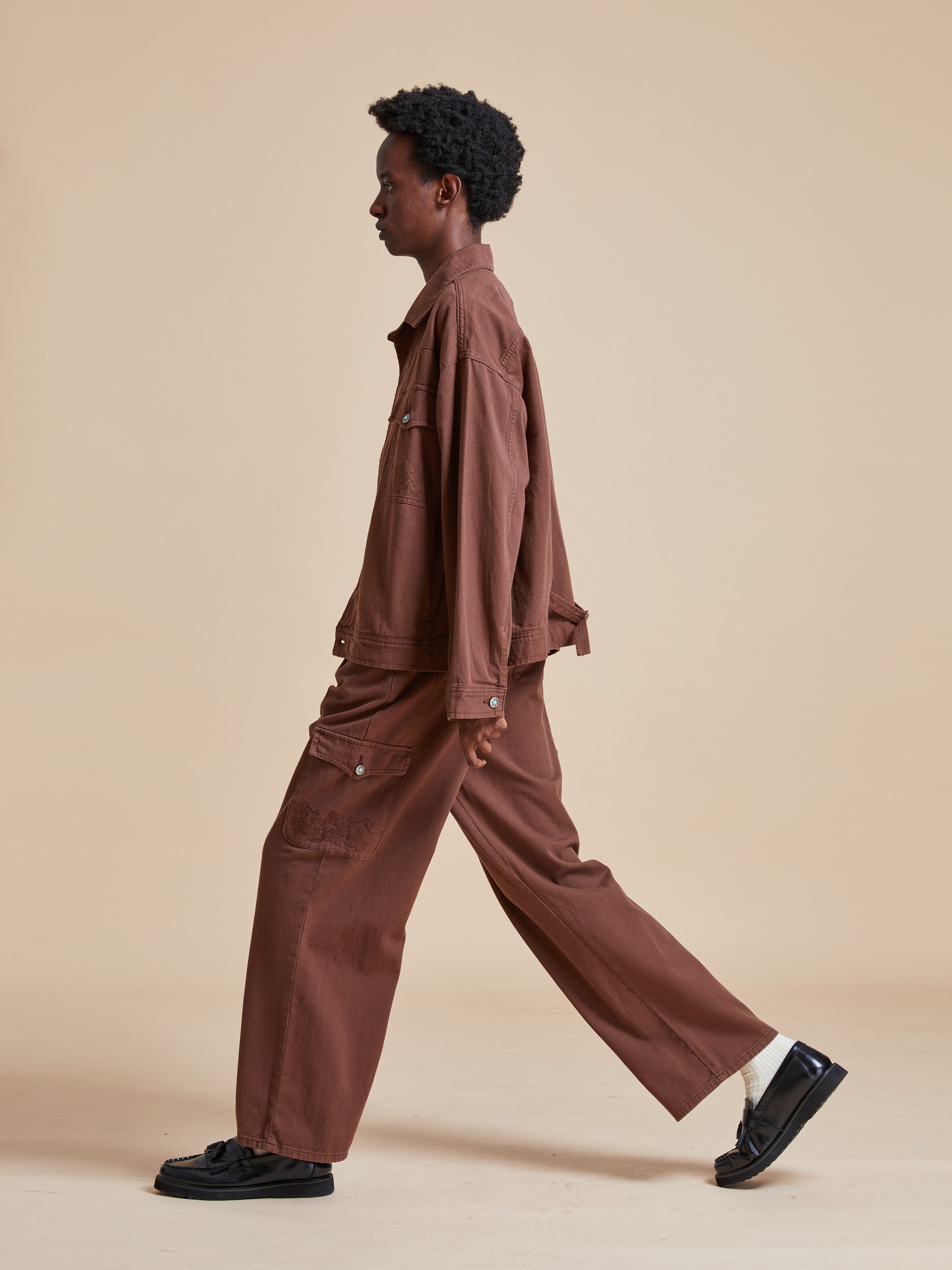 A model in Dusky Western Cargo Jeans walking on a beige background.