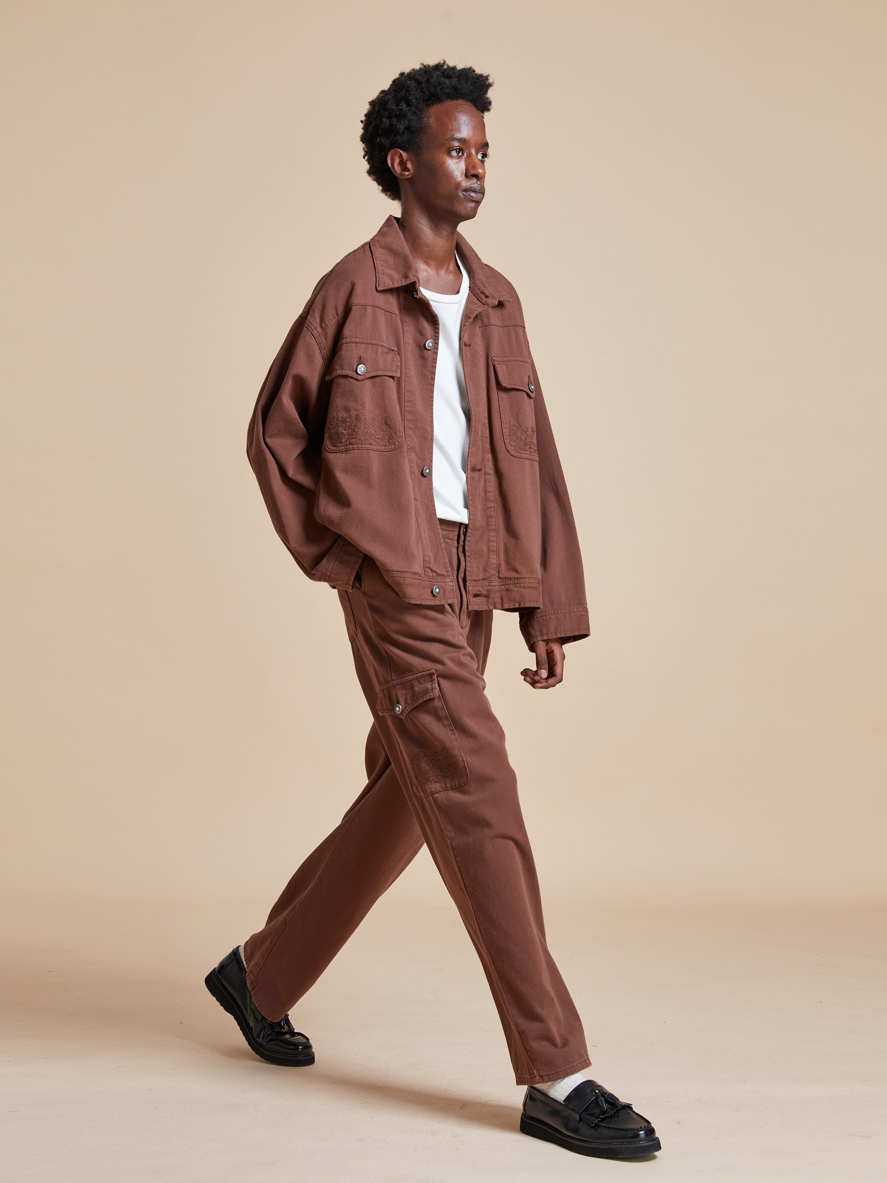 A man in Dusky Western Cargo Jeans by Found and a white t-shirt walking on a beige background.