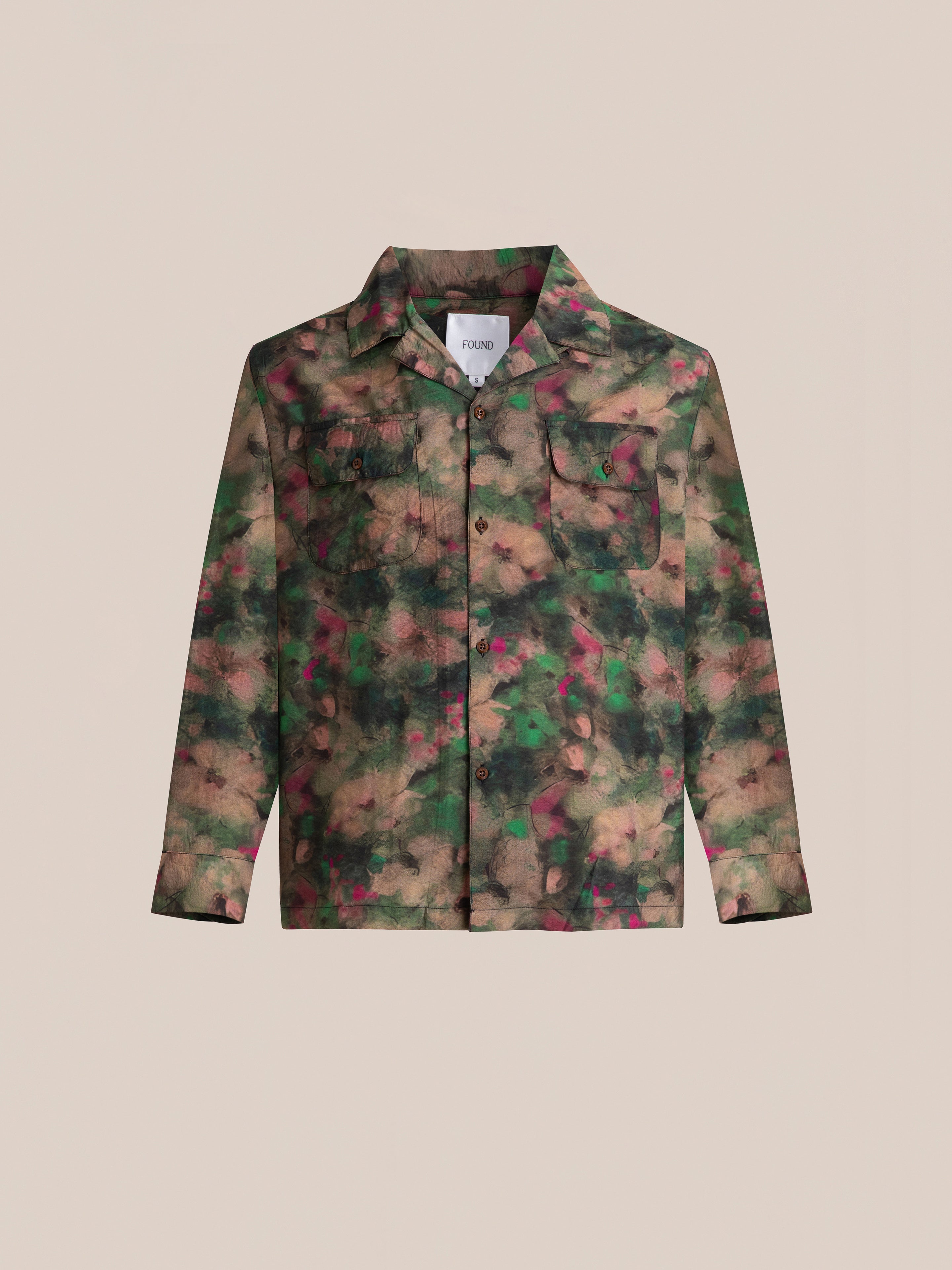 Introducing the Charlot LS Camp Shirt by FOUND, a stylish button-up with a camouflage pattern in shades of green, brown, and pink. This shirt features dual chest pockets and is displayed on a beige background.