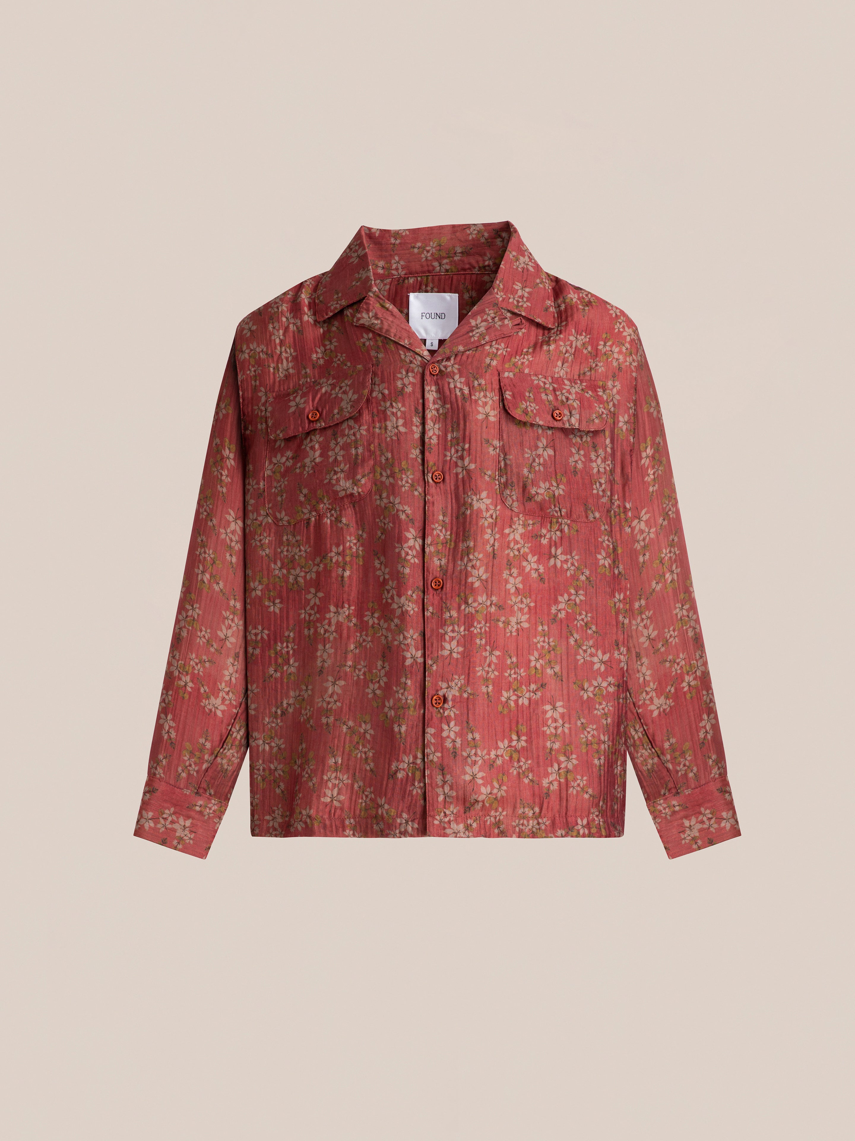 The Charlot LS Camp Shirt by FOUND, featuring a striking red floral pattern and dual chest pockets, stands out beautifully on a plain beige background.