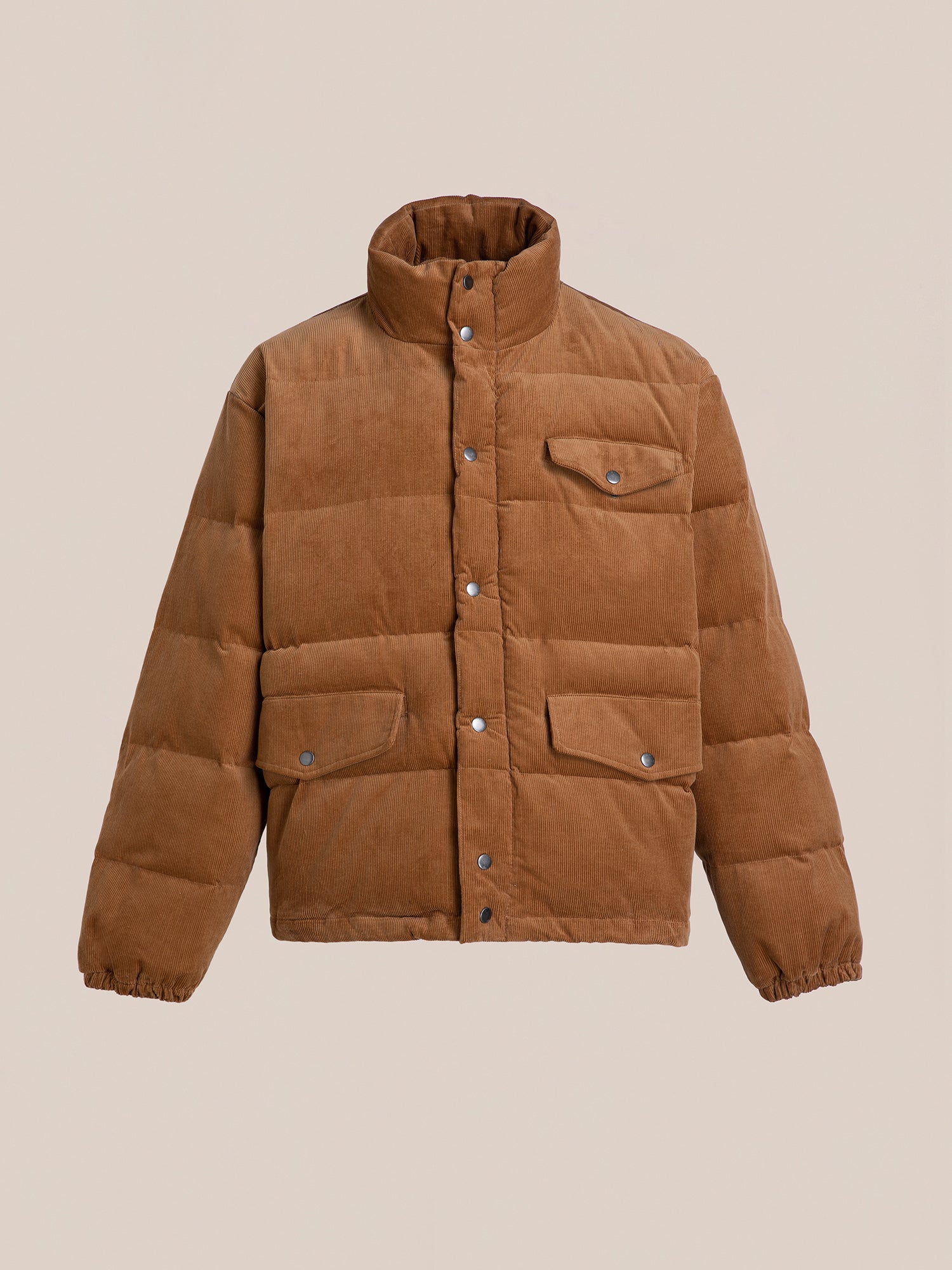 The Corduroy Puffer Jacket by FOUND is designed in a warm tan hue, featuring a high collar, snap buttons, and front flap pockets against a neutral background.