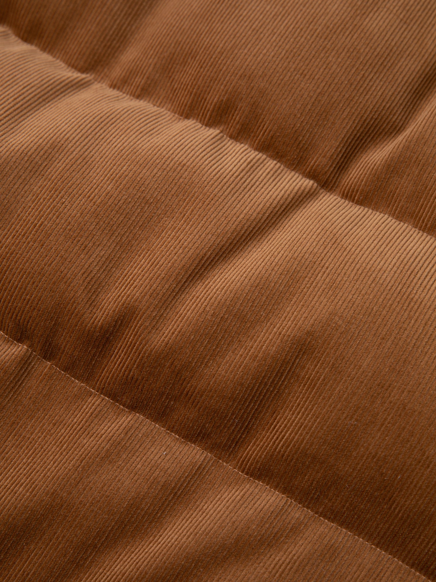 Close-up image of the FOUND Corduroy Puffer Jacket, showcasing its quilted brown corduroy fabric with visible stitching, reminiscent of a warm tan color ideal for cozy comfort.