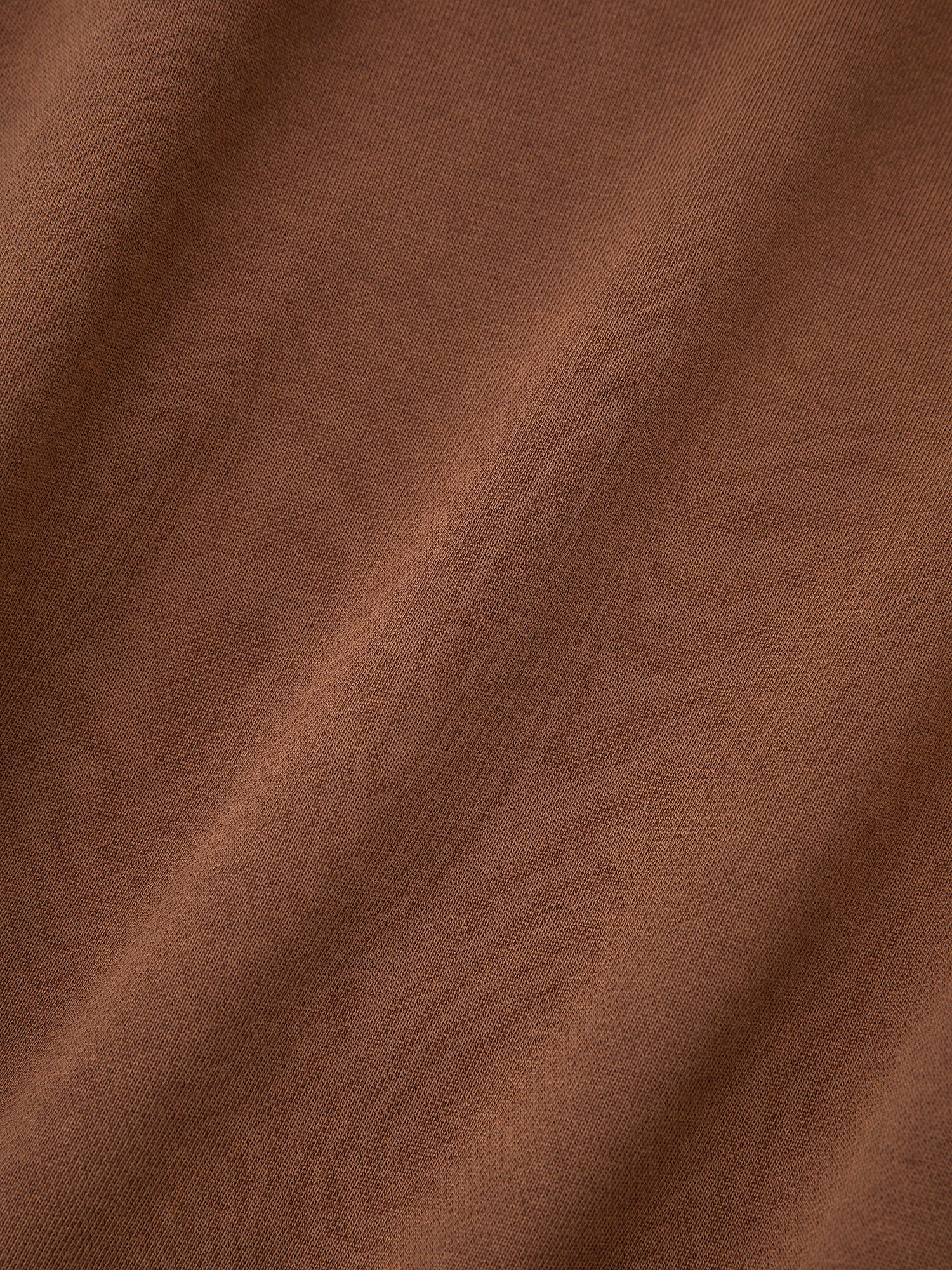 A close-up of the brown fabric from the Tapestry Patchwork Zip Up Hoodie by FOUND, highlighting its smooth, even texture with subtle diagonal folds reminiscent of a South Asian tapestry.