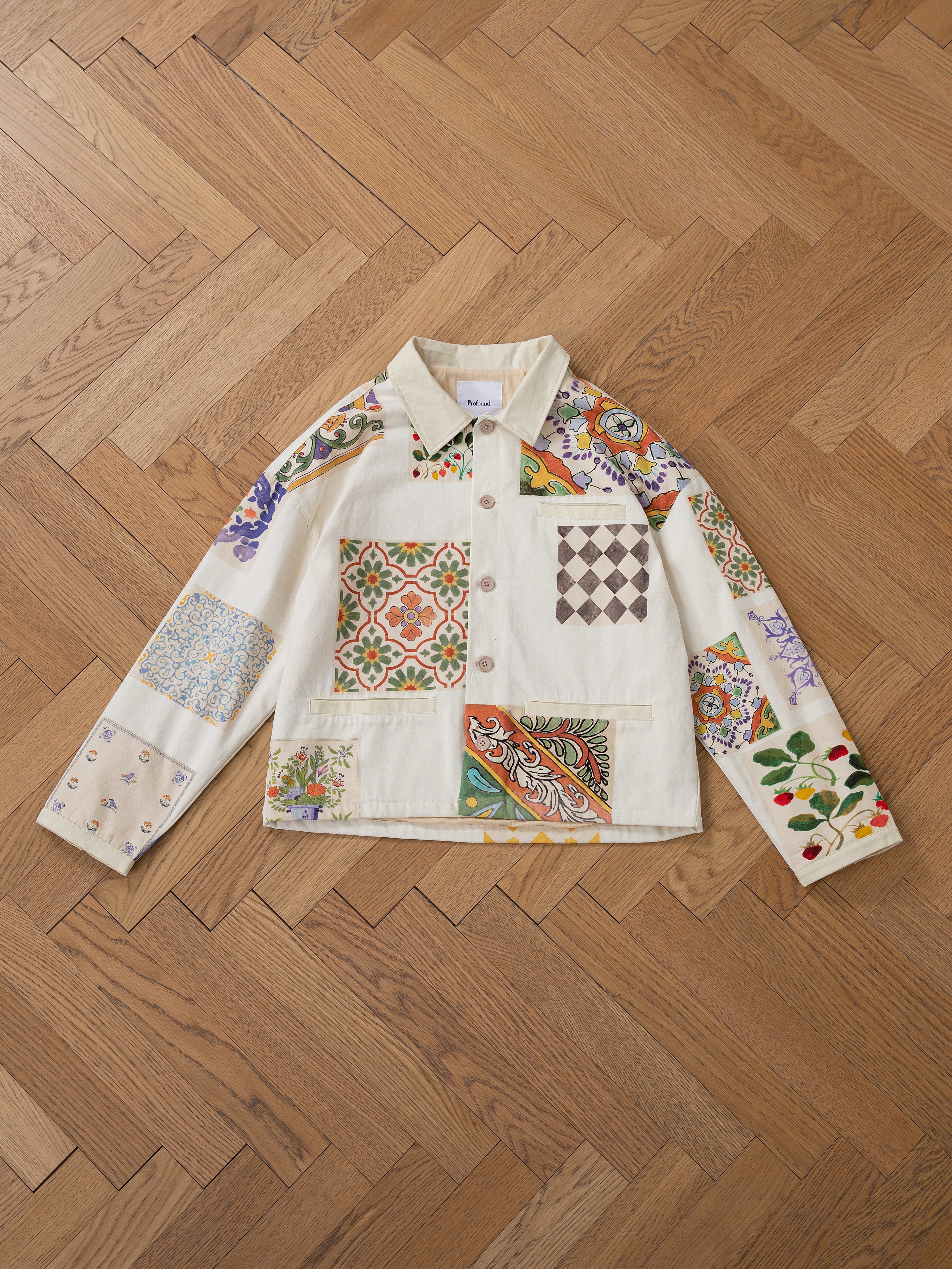 A FOUND Mosaic Work Jacket featuring an array of colorful patterns is spread out on a wooden parquet floor.