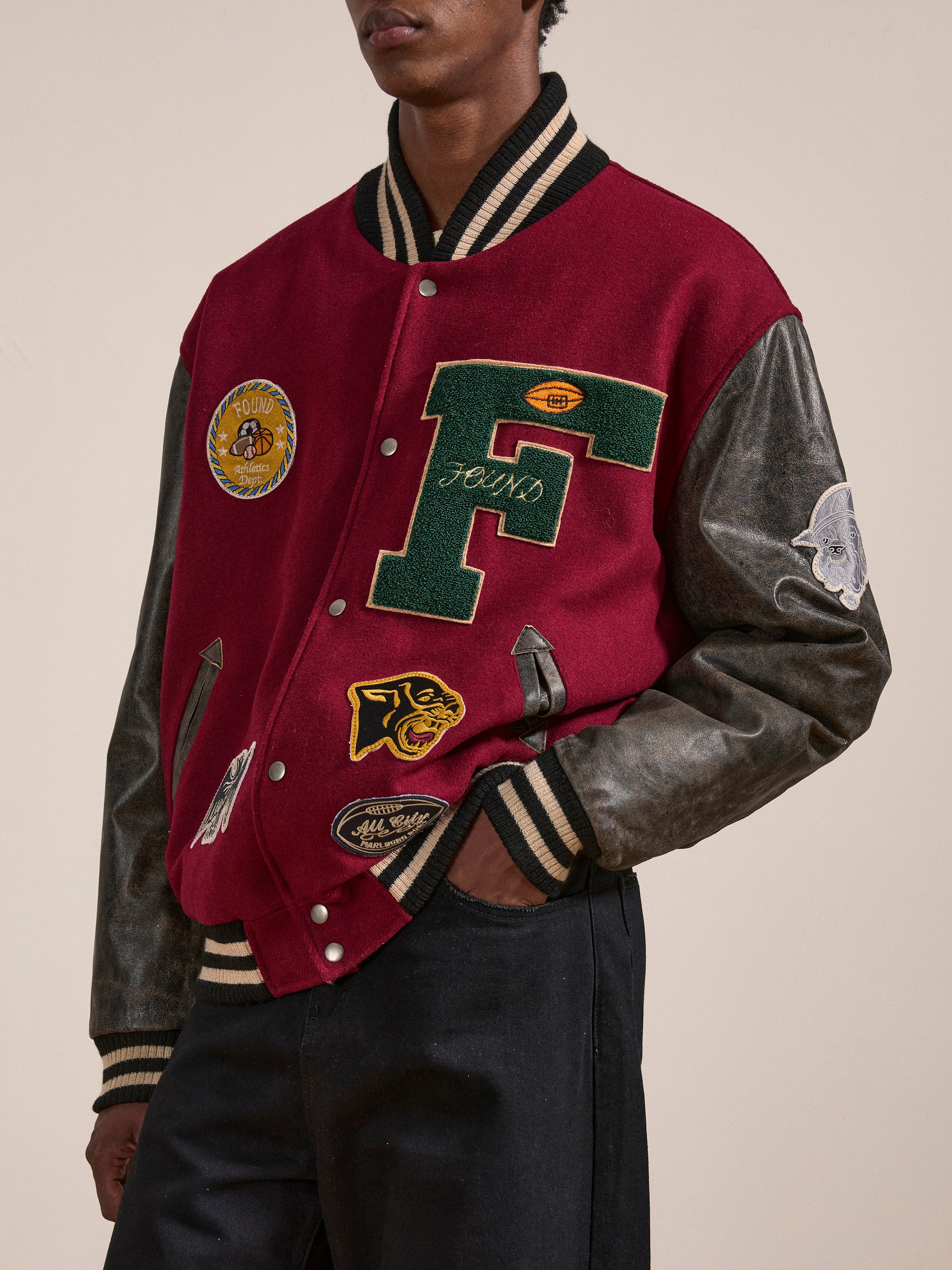 Person wearing Found's Crimson Letterman Jacket, which boasts a vintage look with multiple patches, including a large green 'F', standing against a plain background.