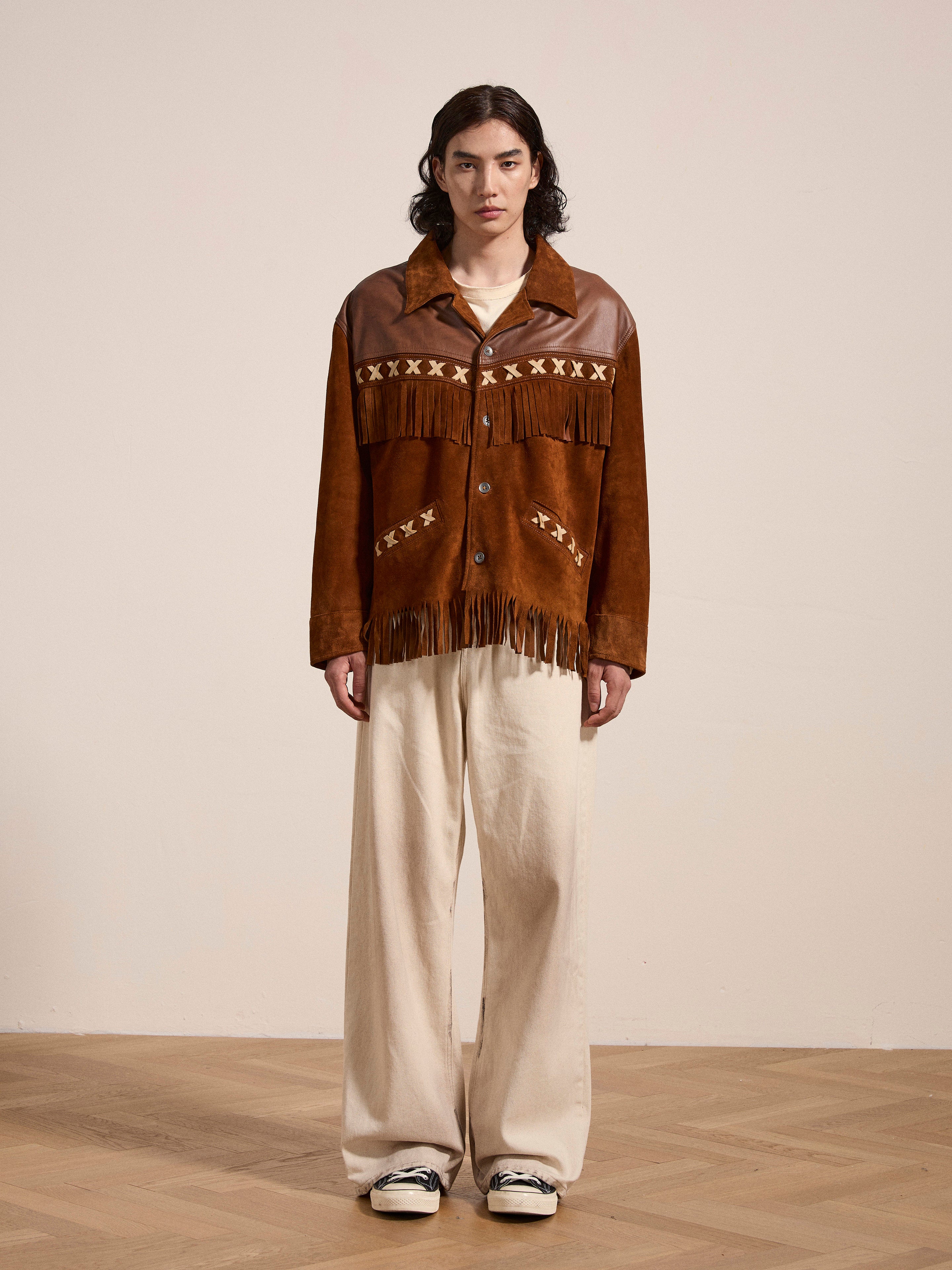 A person wears a FOUND Western Fringe Suede Leather Jacket made from ethically sourced materials, paired with intricate designs and beige wide-leg pants, set against a plain background.