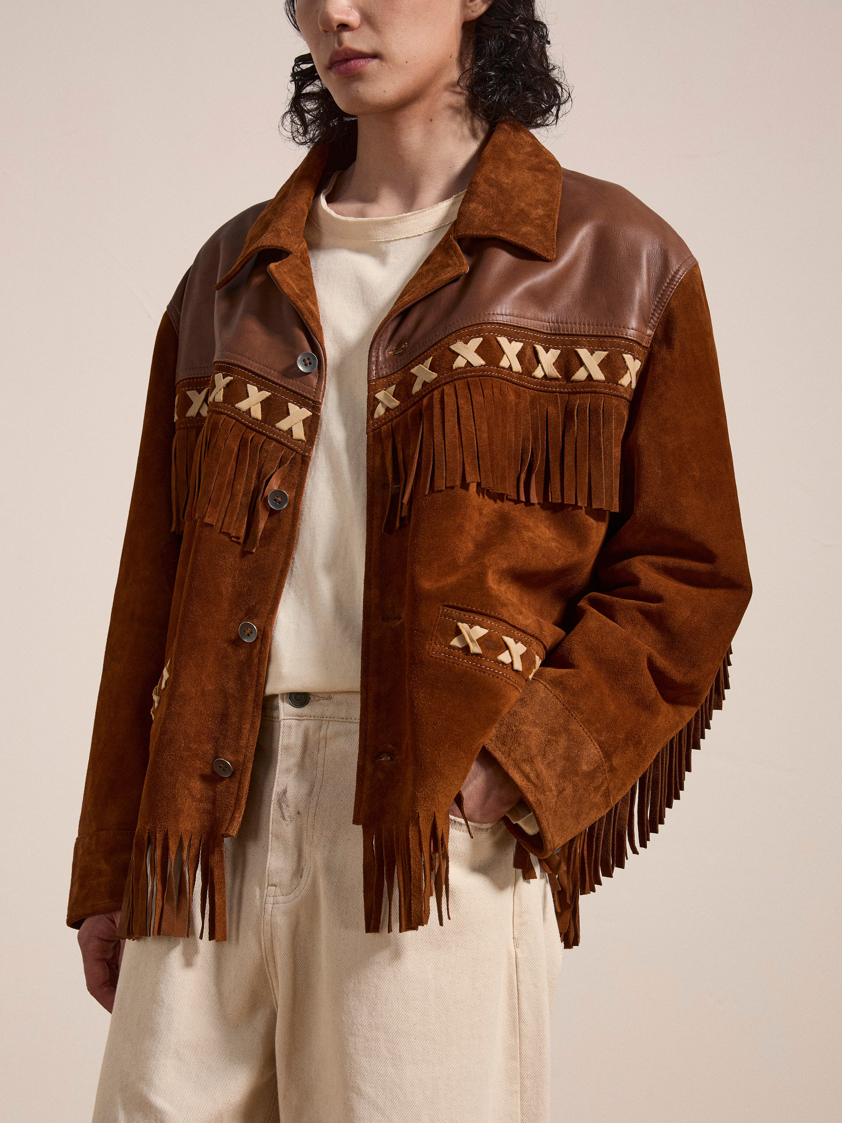 A person wearing a FOUND Western Fringe Suede Leather Jacket, featuring cross-stitch details, paired with a cream shirt and beige pants.