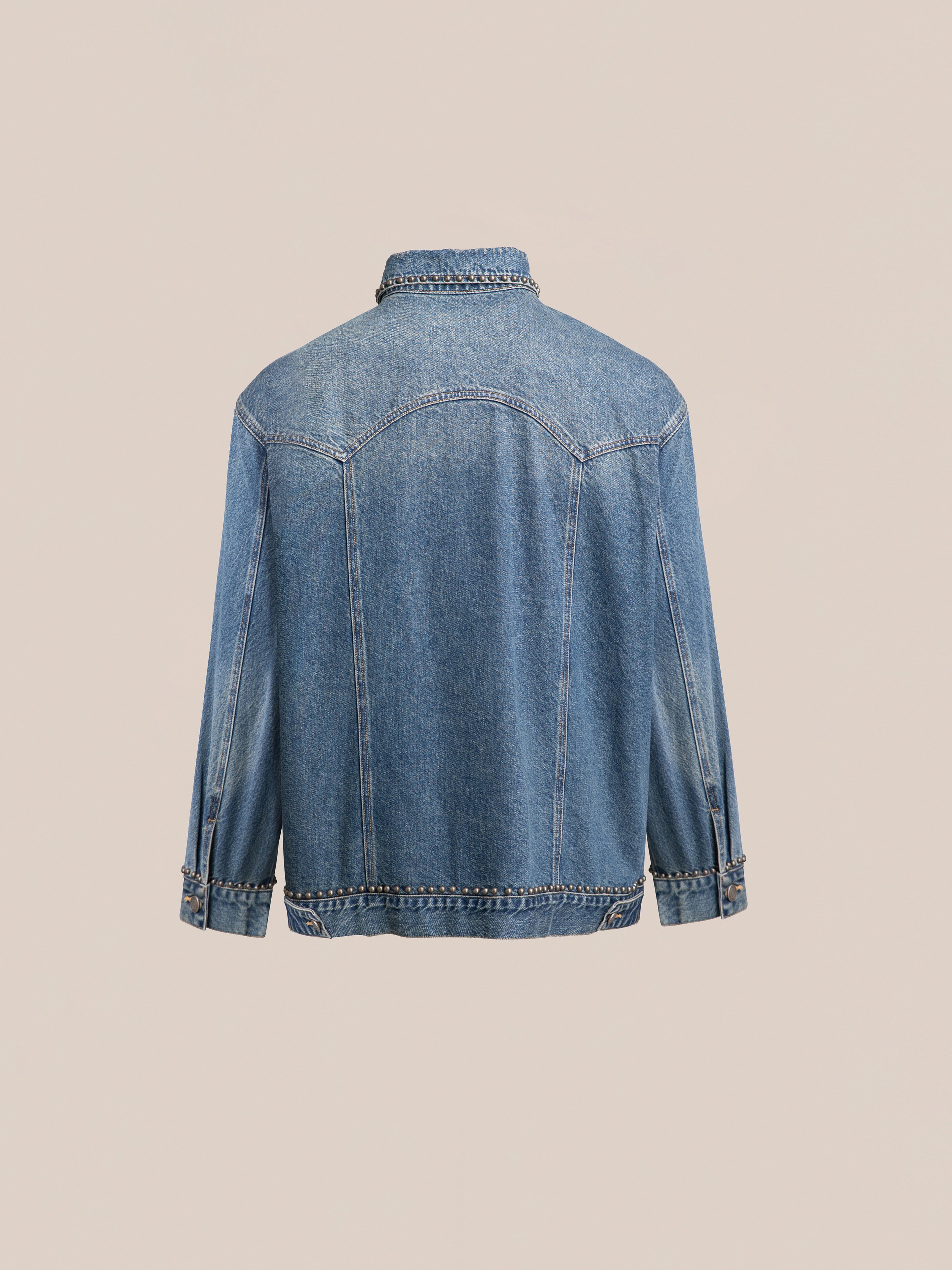 Back view of the FOUND Azar Studded Denim Trucker Jacket in vintage blue wash, featuring long sleeves and buttoned cuffs, displayed against a plain beige background.