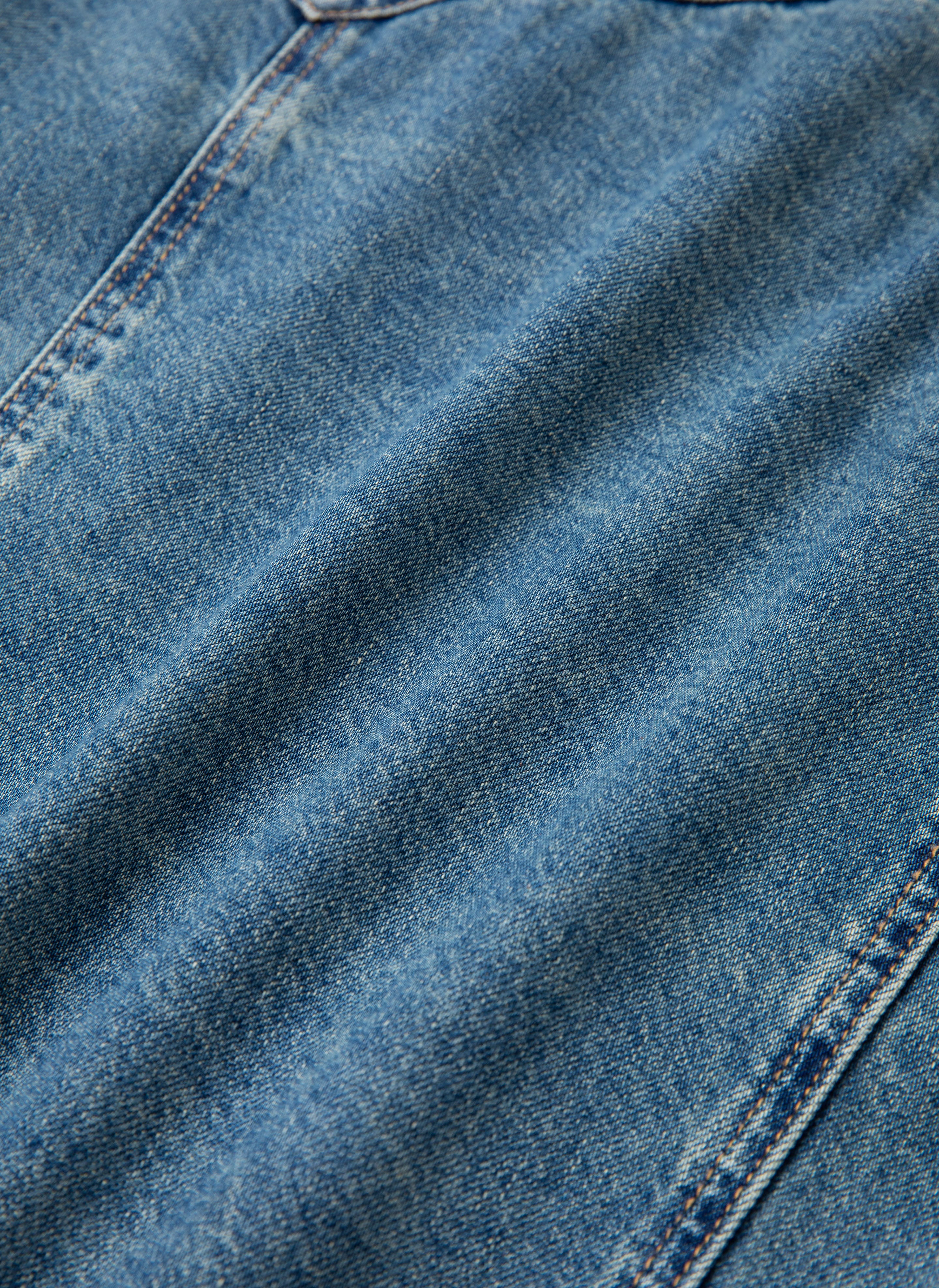 Close-up of vintage blue wash denim fabric, showing texture and stitching, reminiscent of the Azar Studded Denim Trucker Jacket by FOUND.