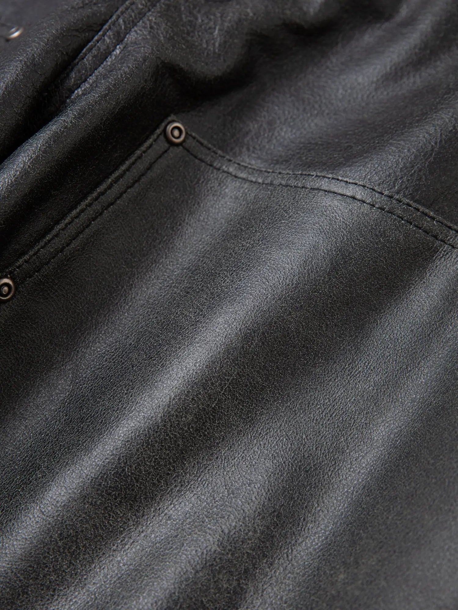 Close-up of the Distressed Genuine Leather Carpenter Pants by FOUND, showcasing visible stitching and rivets near a pocket seam, reminiscent of ethically sourced black leather garments.