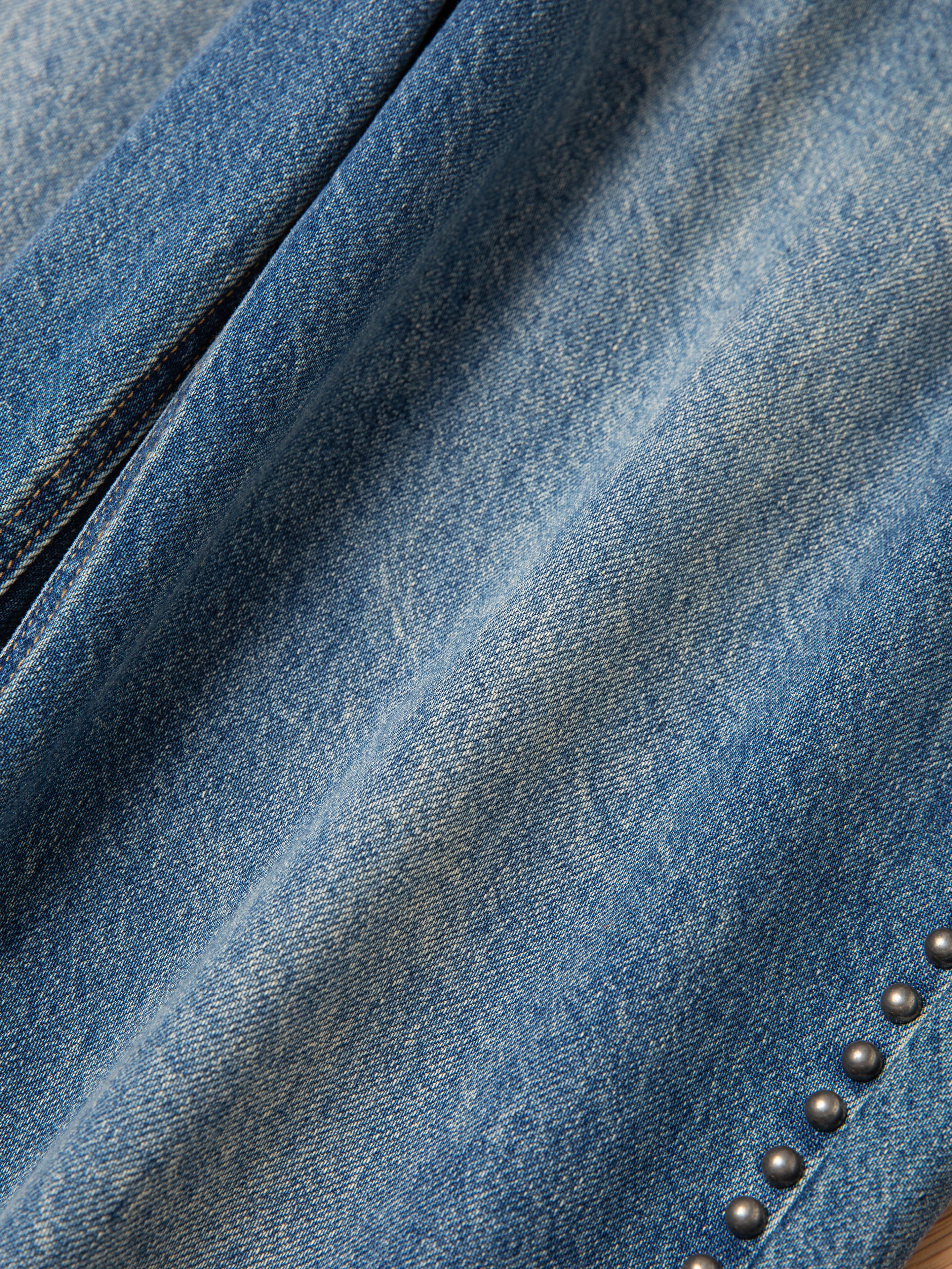 Close-up of the Azar Studded Jeans by FOUND, featuring vintage blue wash denim fabric with antique matte silver studs accenting the edge.