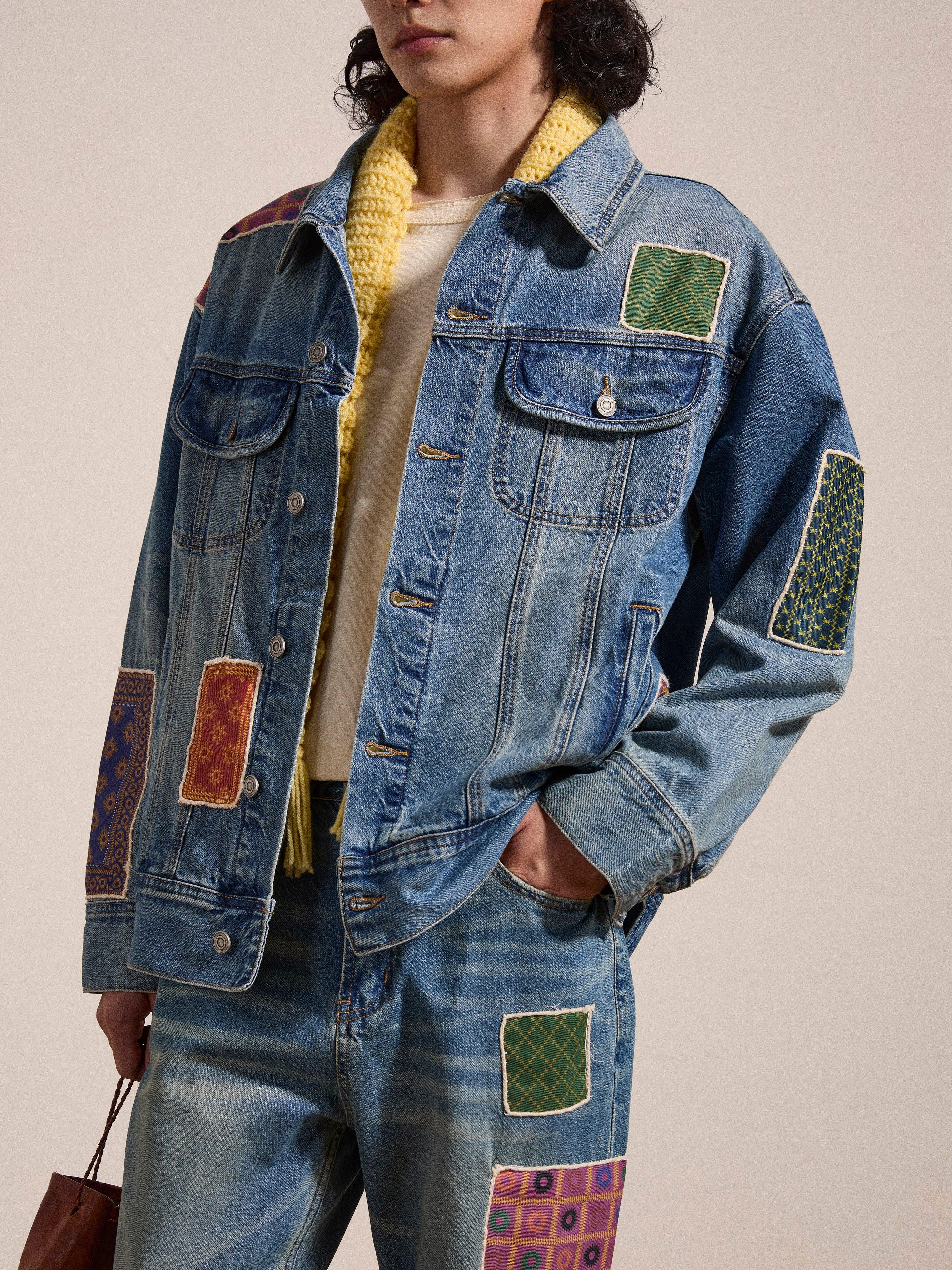 A person wearing the FOUND Kantha Patchwork Denim Trucker Jacket with matching jeans, holding a bag.