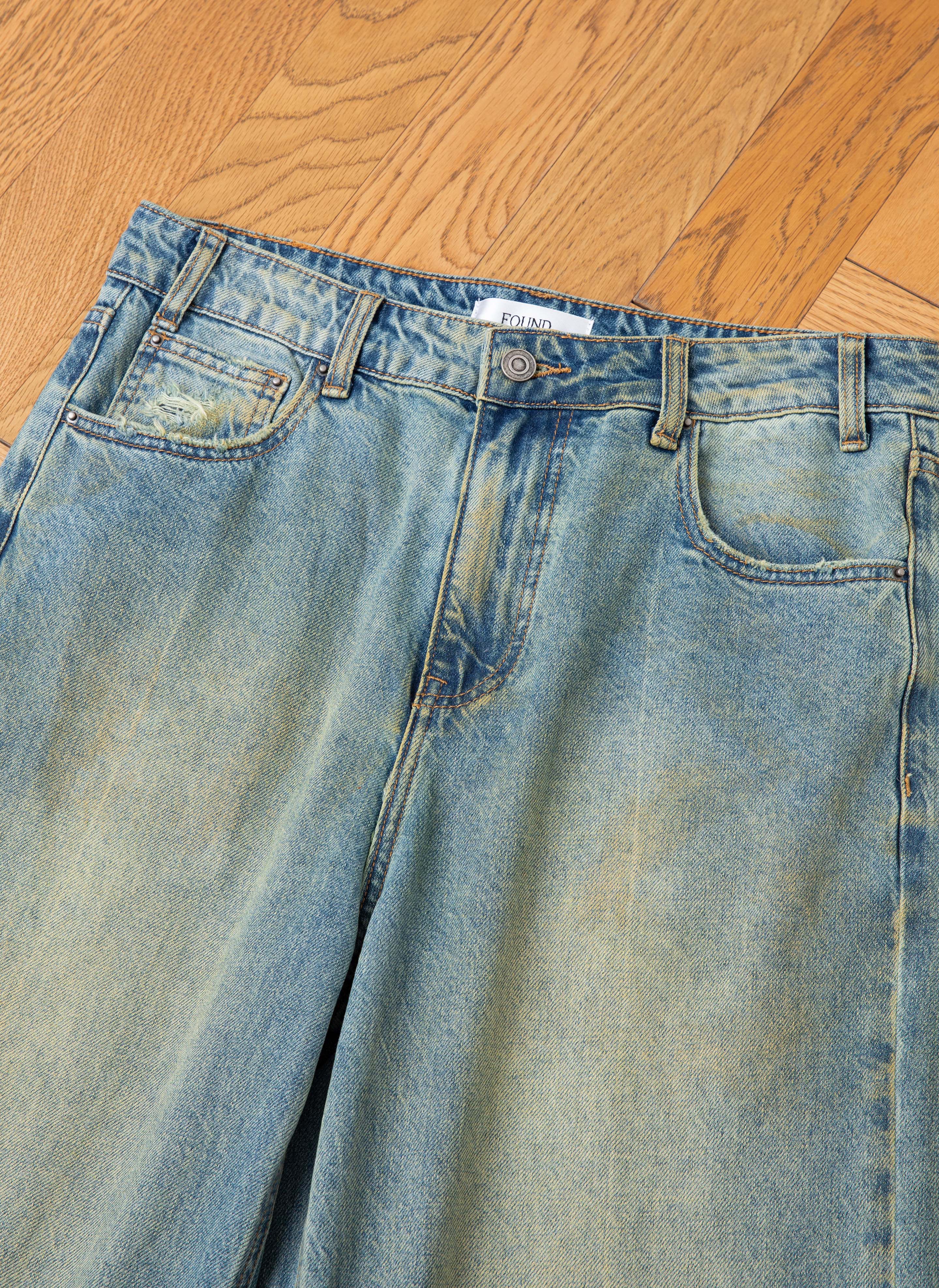 FOUND's Lacy Baggy Jeans, a pair of light blue denim with a button and zipper fly and subtle distressing, displayed flat on a wooden surface.