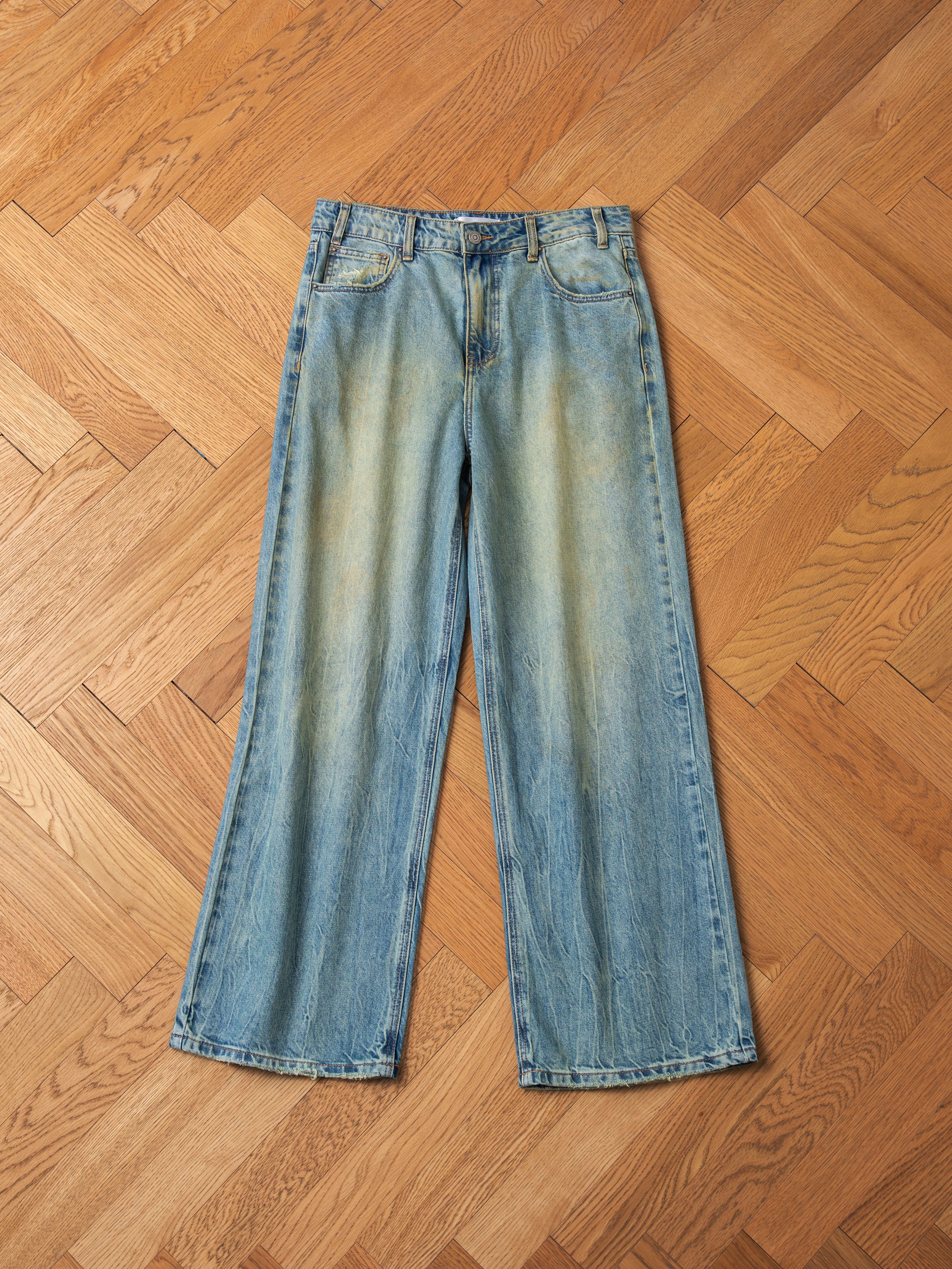 A pair of Lacy Baggy Jeans by FOUND in a dirty blue wash with light distressing laid flat on a hardwood floor.