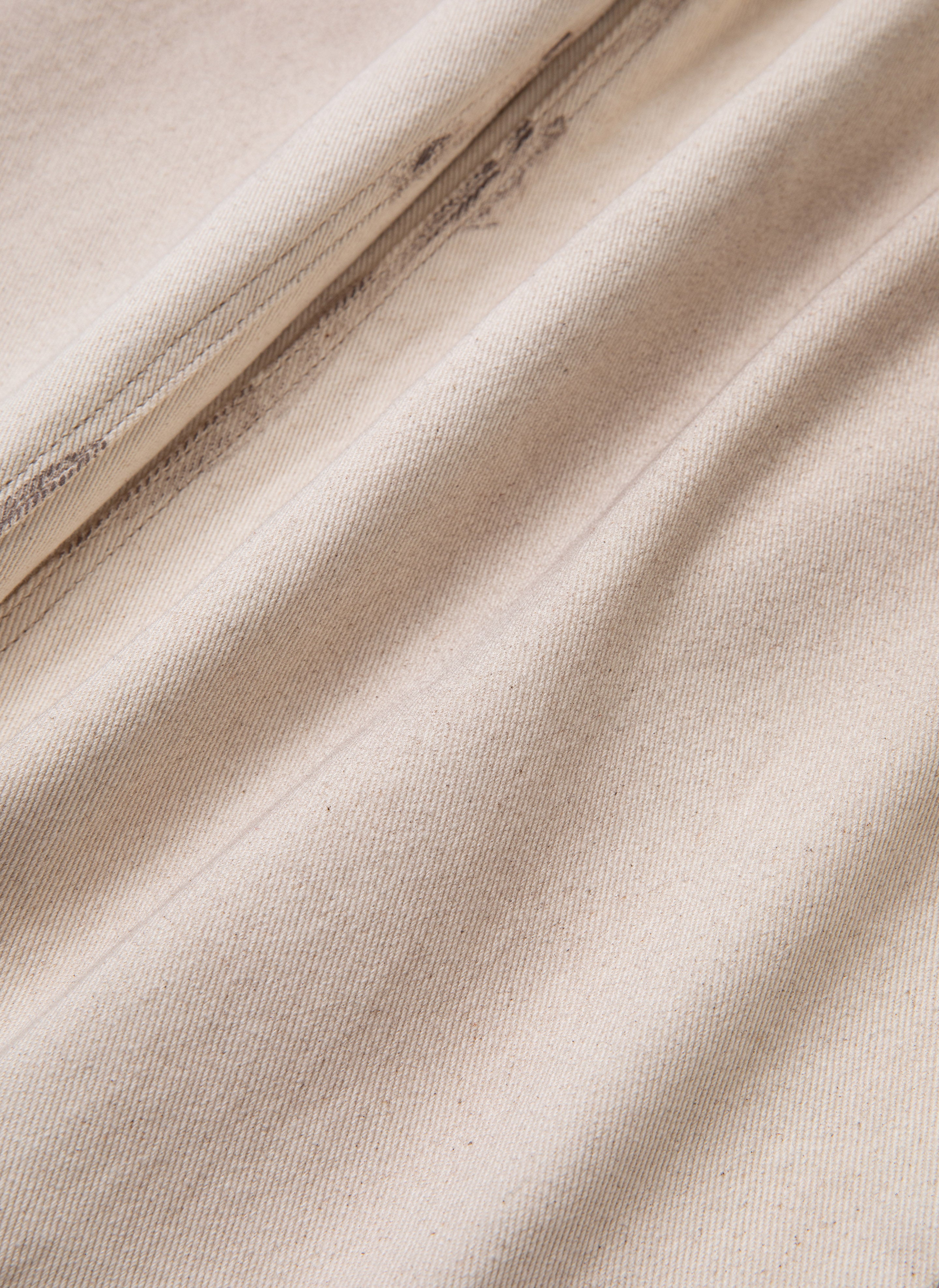 Close-up of beige, slightly wrinkled fabric with diagonal lines indicating the weave pattern, reminiscent of the Lacy Baggy Jeans from FOUND in a dirty white wash.