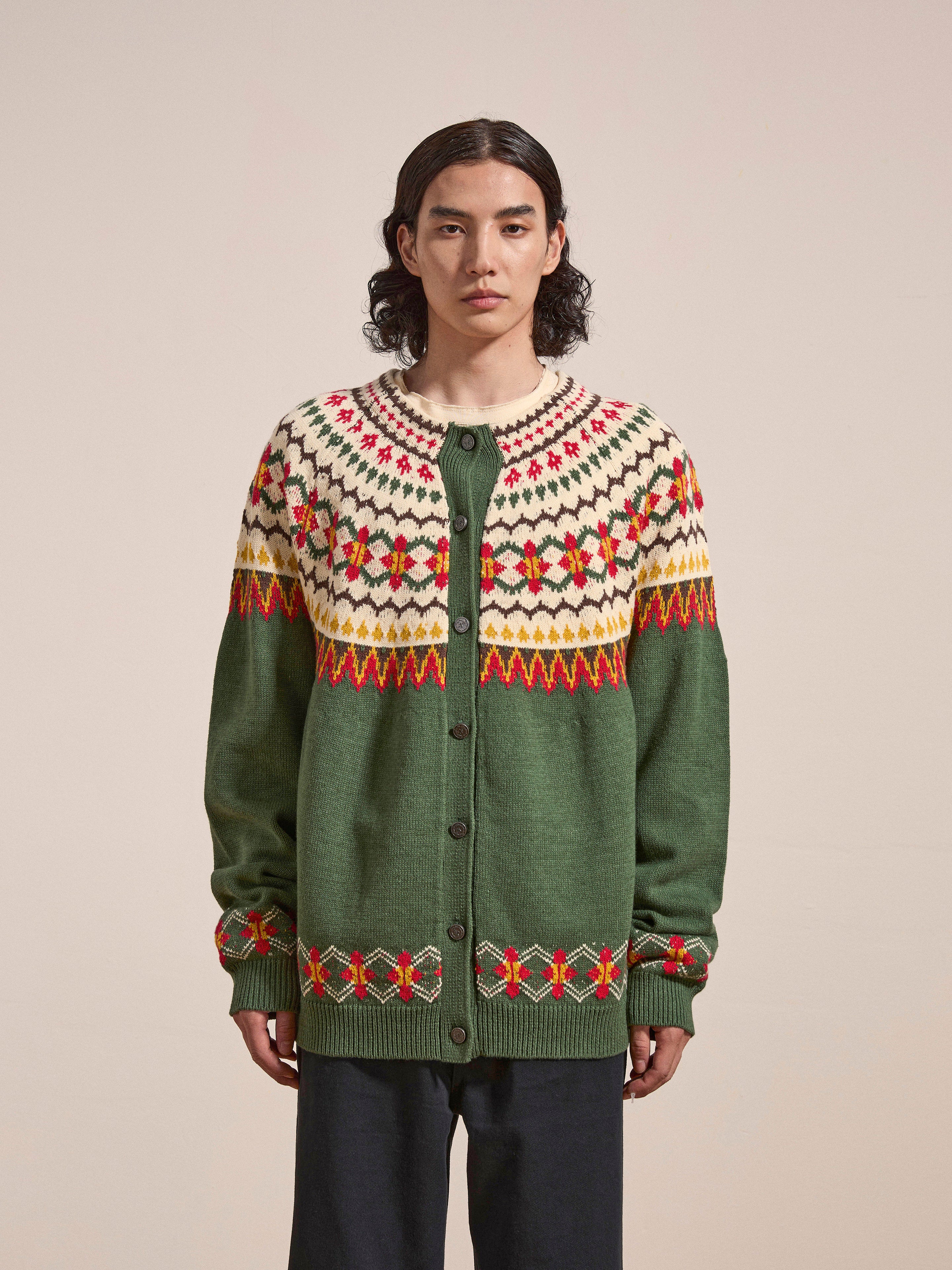 Person with long dark hair, wearing the oversized Jahan Isles Knit Cardigan by FOUND, featuring a green and cream Scottish Fair Isle design with red accents and antique silver buttons, standing against a plain background.