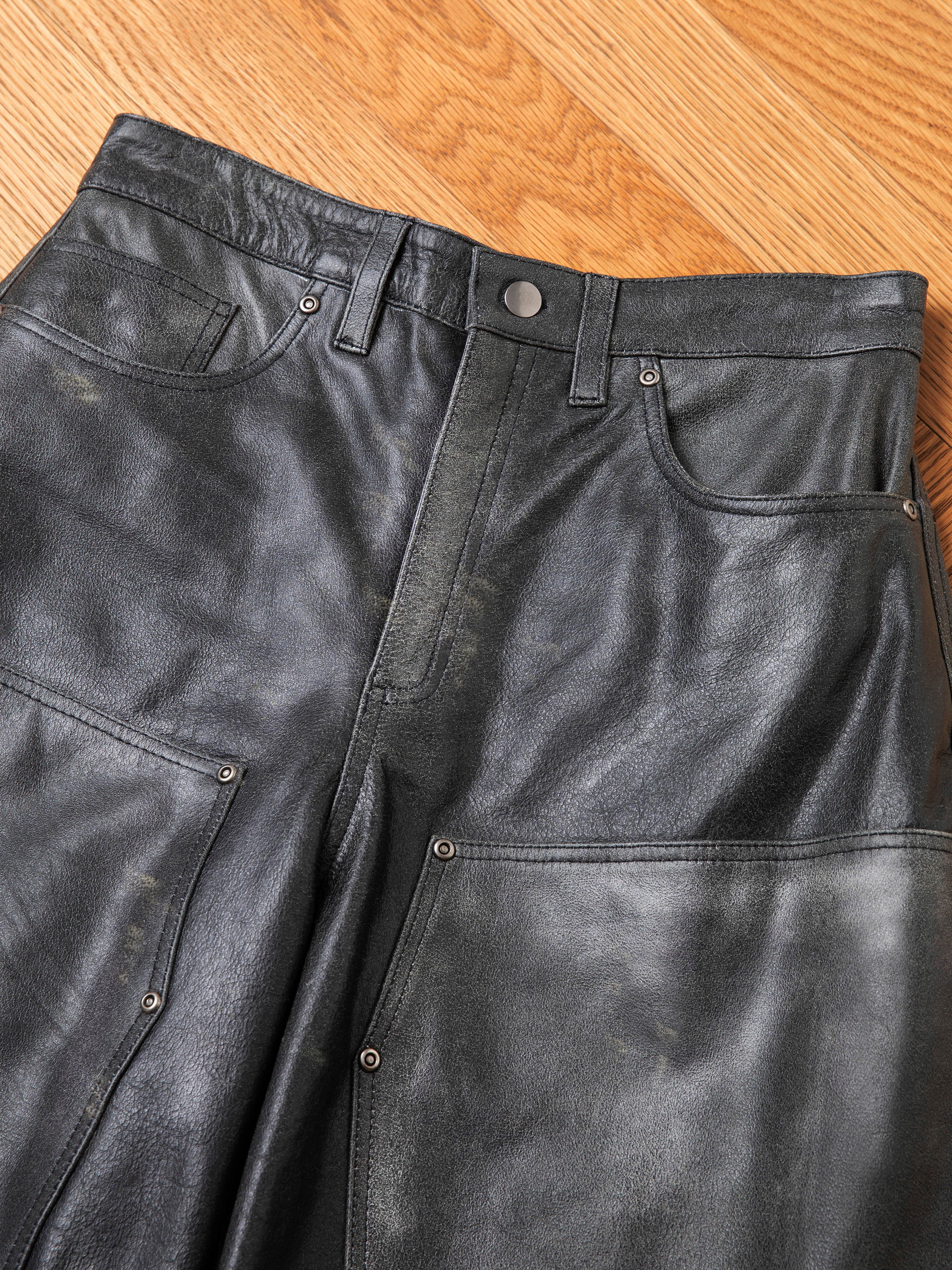 The FOUND Distressed Genuine Leather Carpenter Pants, featuring a double-knee silhouette, front pockets, belt loops, and rivet details, are laid flat on a wooden floor.