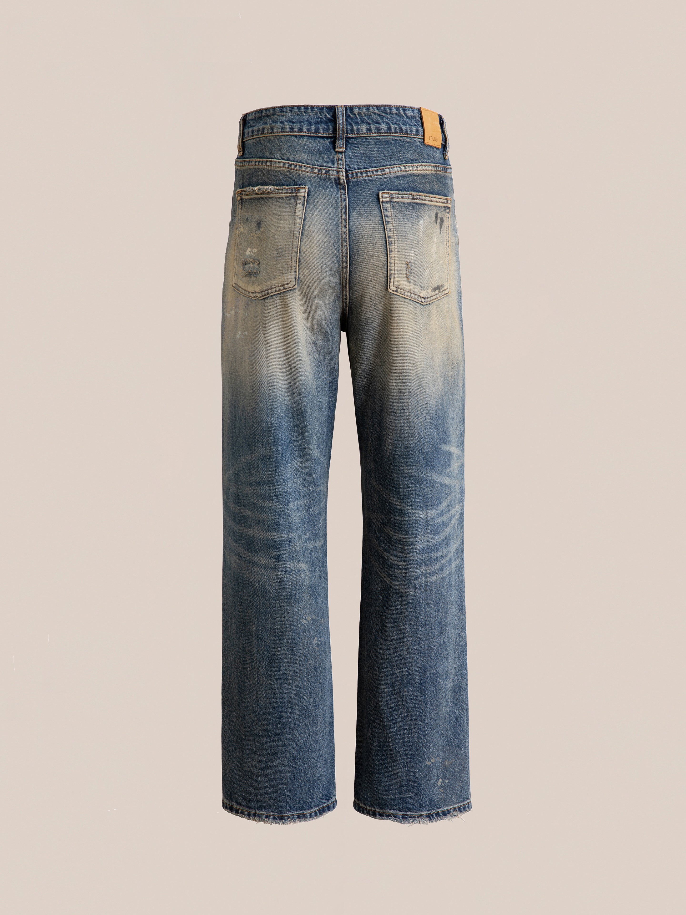 Back view of the Monet Paint Jeans by FOUND, featuring a faded and distressed design, two back pockets, and a leather patch on the waistband, all accentuated by their vintage blue wash.