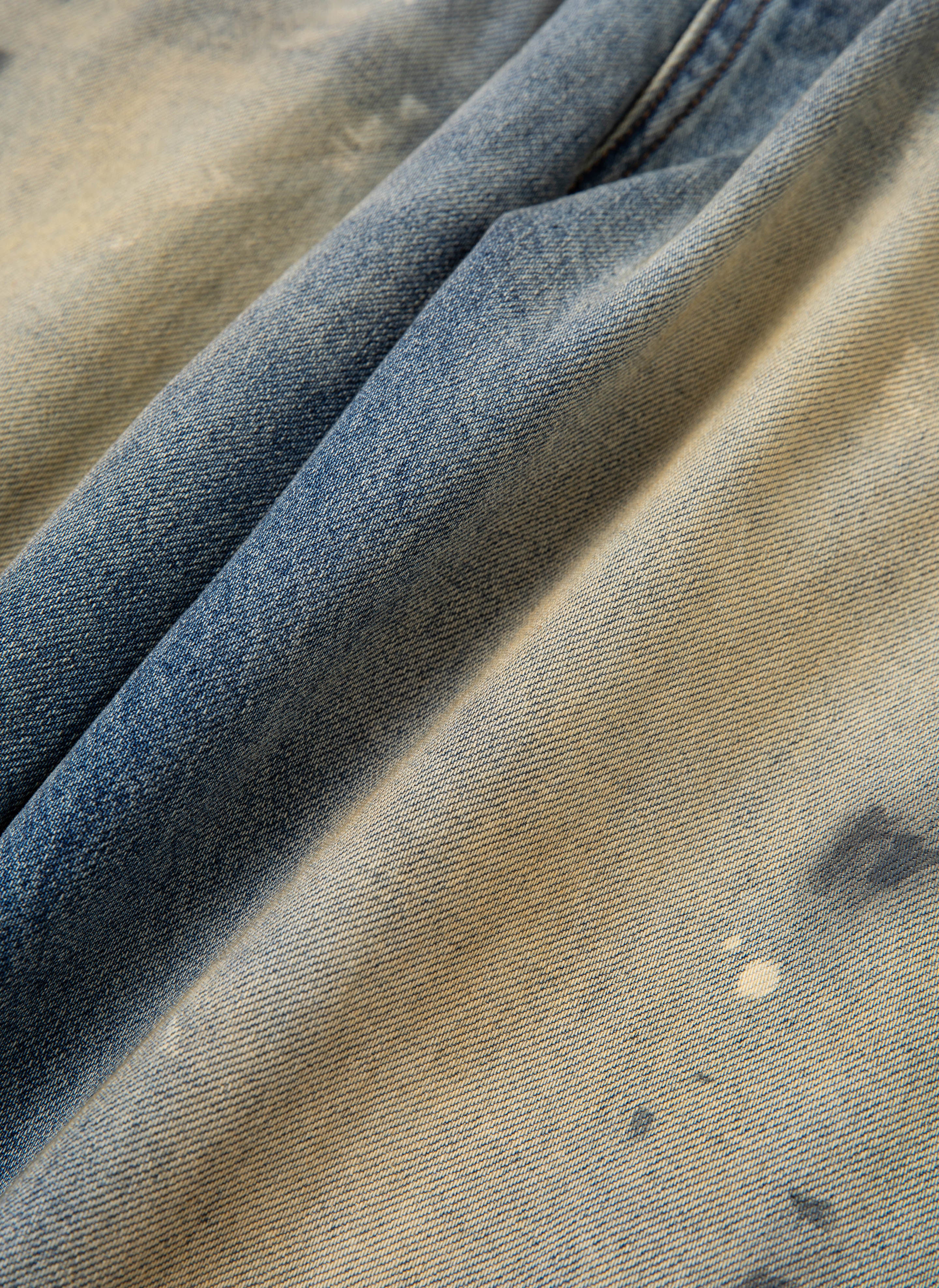 Close-up of a faded, distressed denim fabric with visible signs of wear and discoloration, reminiscent of FOUND's Monet Paint Jeans featuring a vintage blue wash and subtle hand-painted splatter accents.