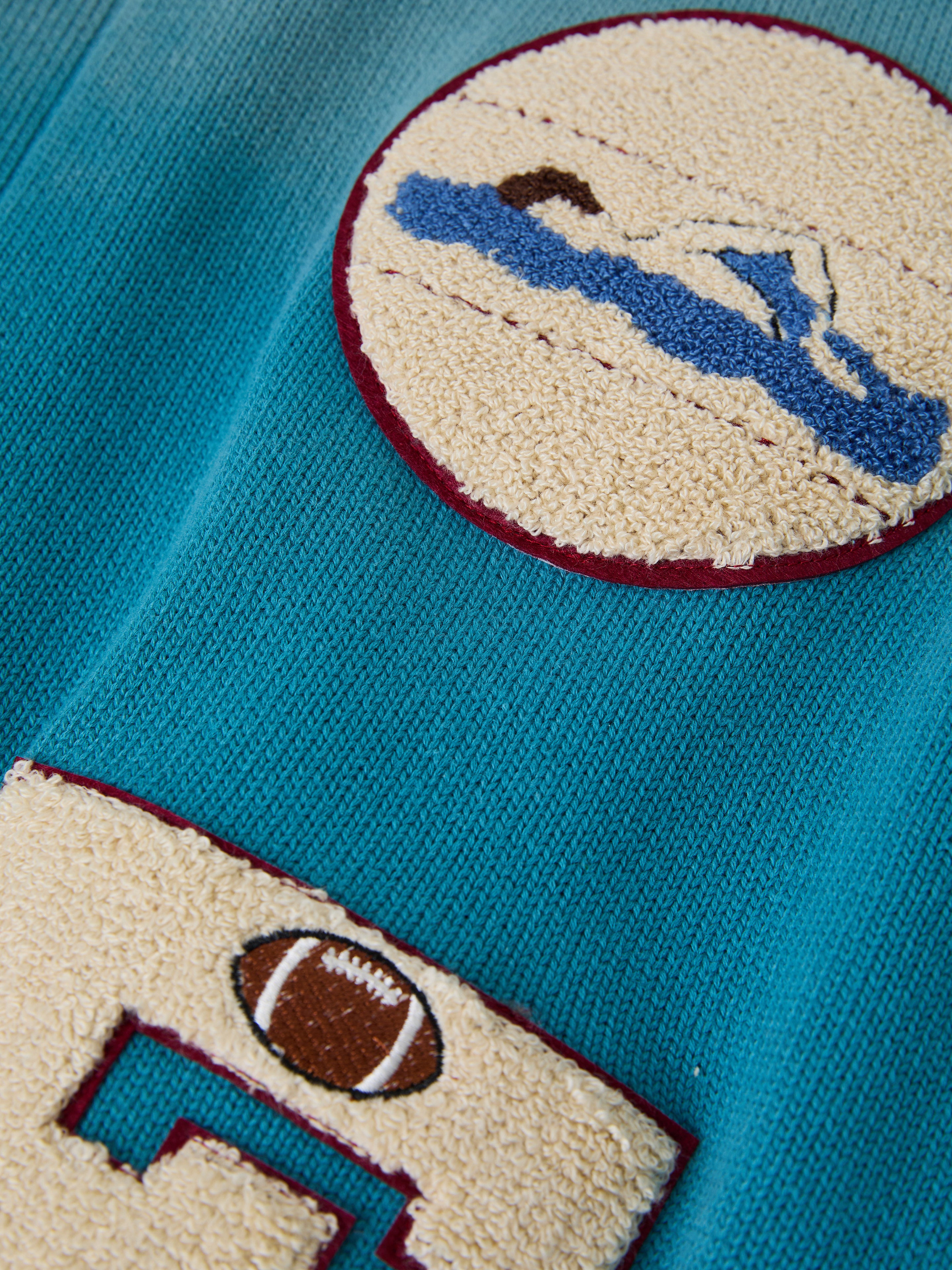 The Fin Varsity Patch Collared Cardigan from FOUND features teal fabric embroidered with patches of a swimmer and football in contrasting hues, delivering a vintage collegiate style.