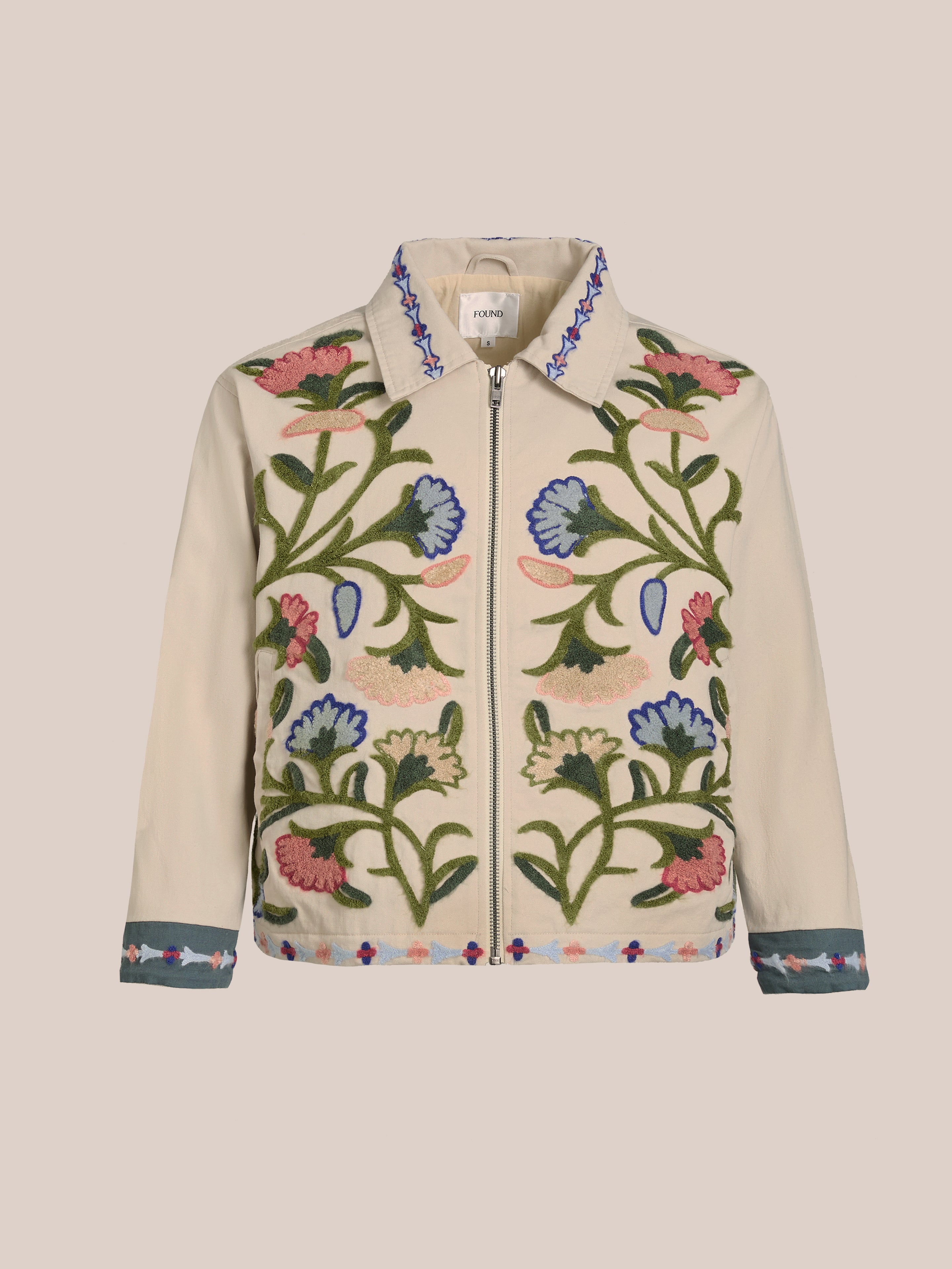 The Floral Embroidered Work Jacket by FOUND is a unisex, relaxed-fit cotton canvas jacket with a front zipper. It features vibrant floral embroidery in green, blue, pink, and red, offering both style and comfort.