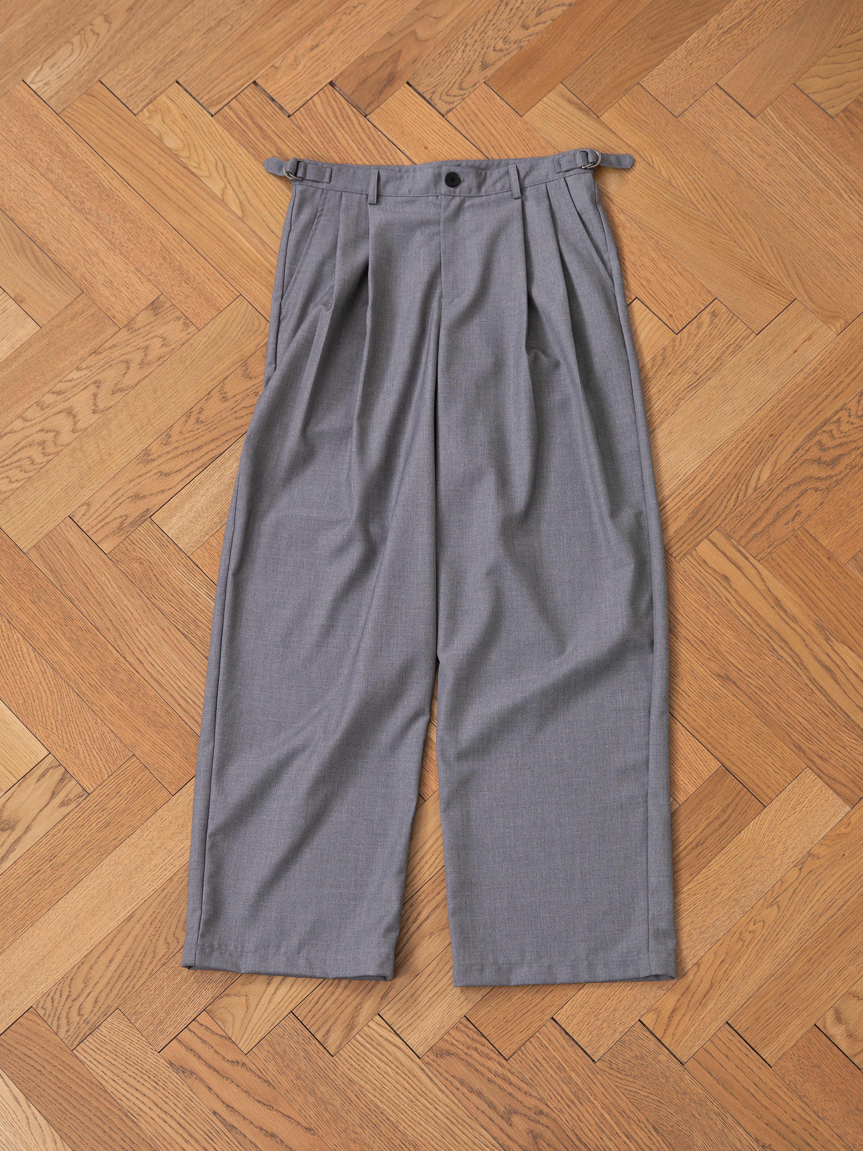 Pleated Trousers in gray from FOUND displayed on a wooden herringbone-patterned floor.