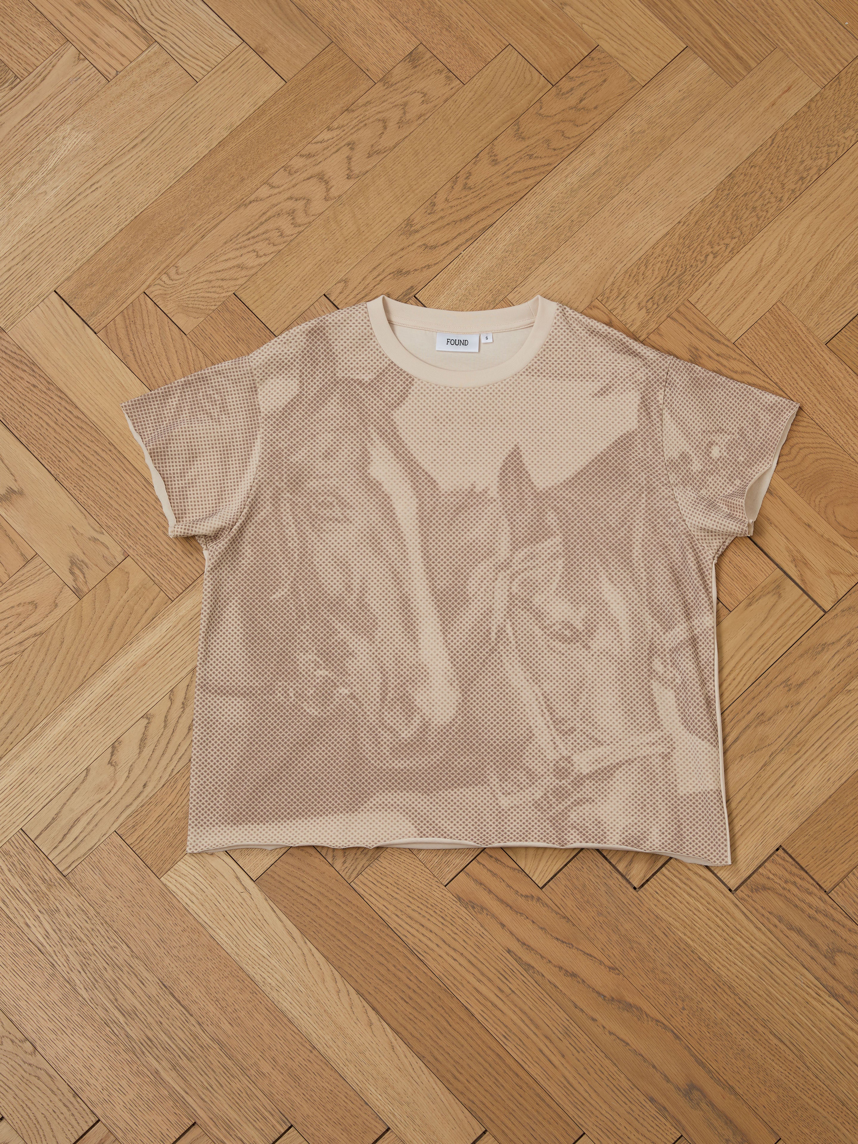 The relaxed-fit Horse Racer Tee by FOUND, featuring a wolf print, rests flat on a herringbone wooden floor, reflecting its equestrian heritage.