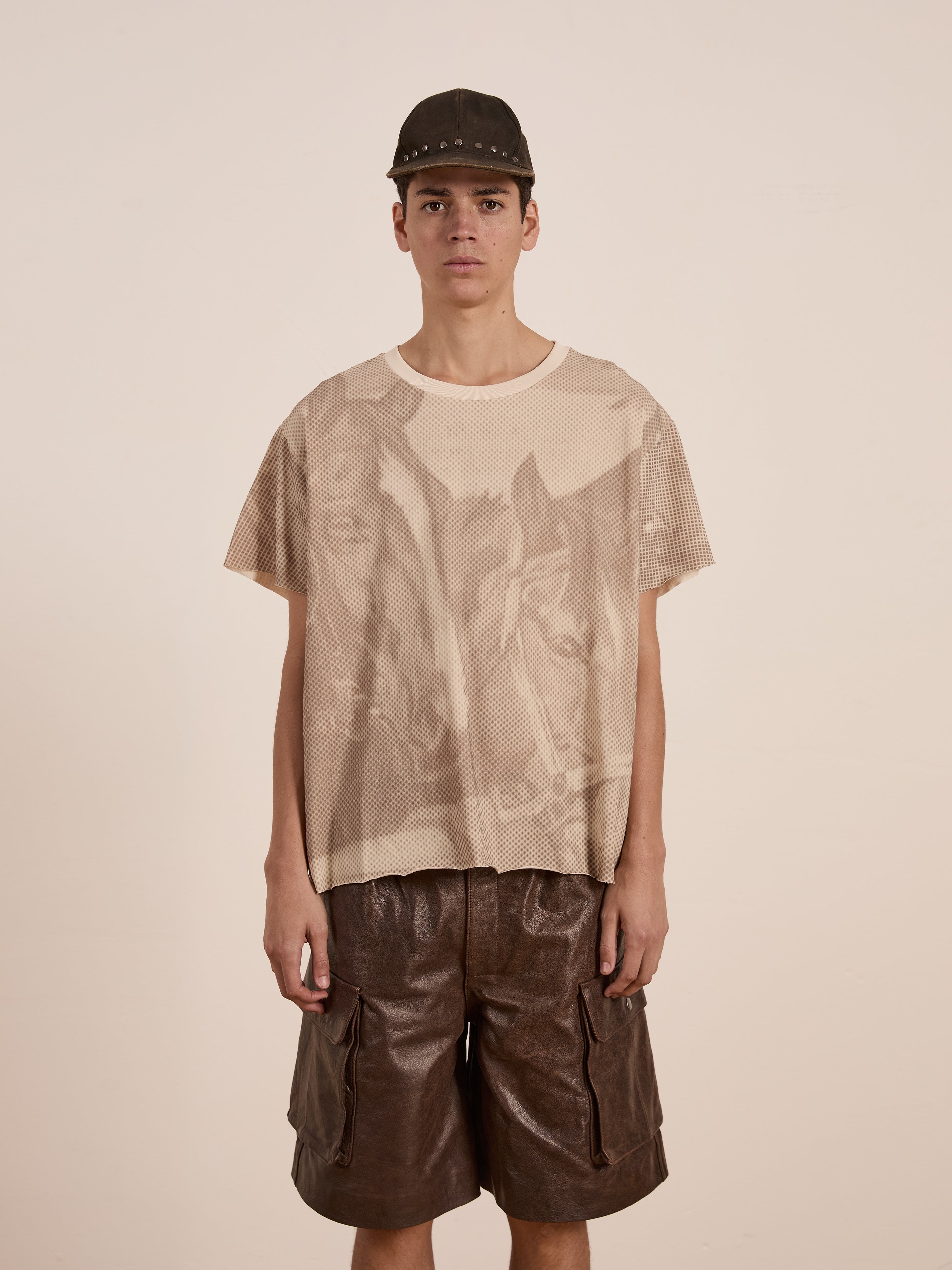 Wearing a Horse Racer Tee by FOUND—a relaxed fit mesh t-shirt with equestrian heritage graphic—someone pairs it effortlessly with brown leather shorts against a plain background.