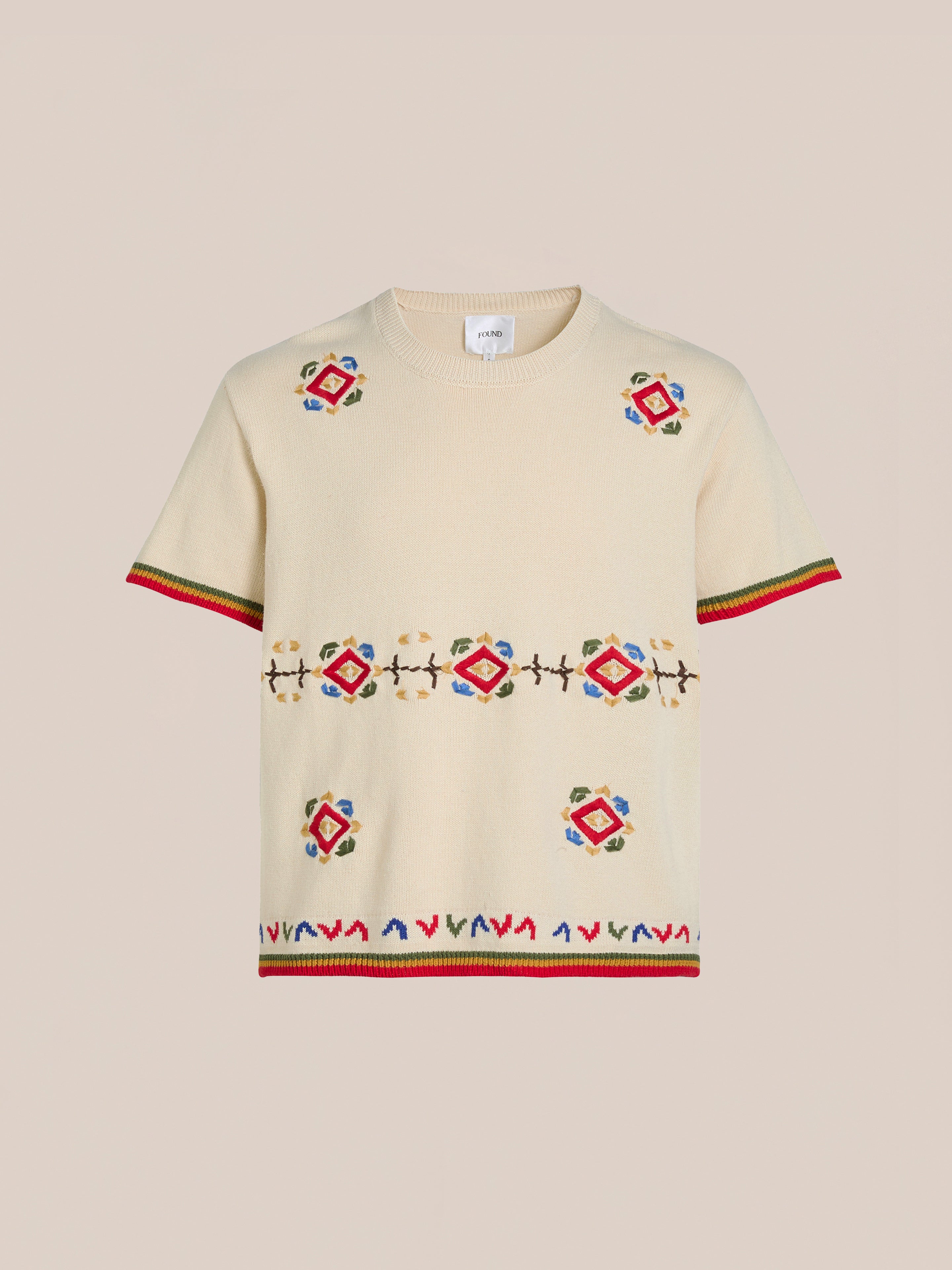 The Knit Flower Petal Tee by FOUND features a beige short-sleeve design with colorful geometric embroidery, red and green striped borders, and jacquard floral motifs offering vintage-inspired charm.