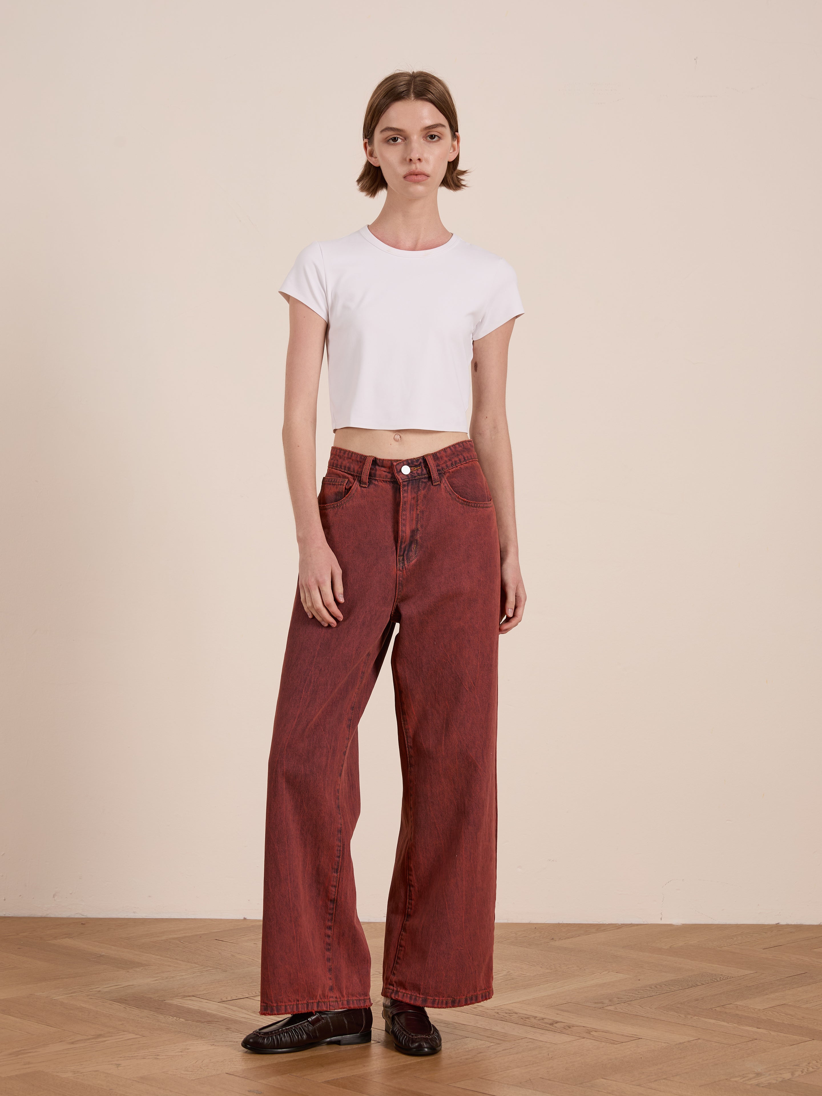 Styled in a white crop top, Lacy Baggy Jeans by FOUND, vintage red wash high-waisted wide-leg silhouette, paired with black shoes, standing on a wooden floor against a plain wall.