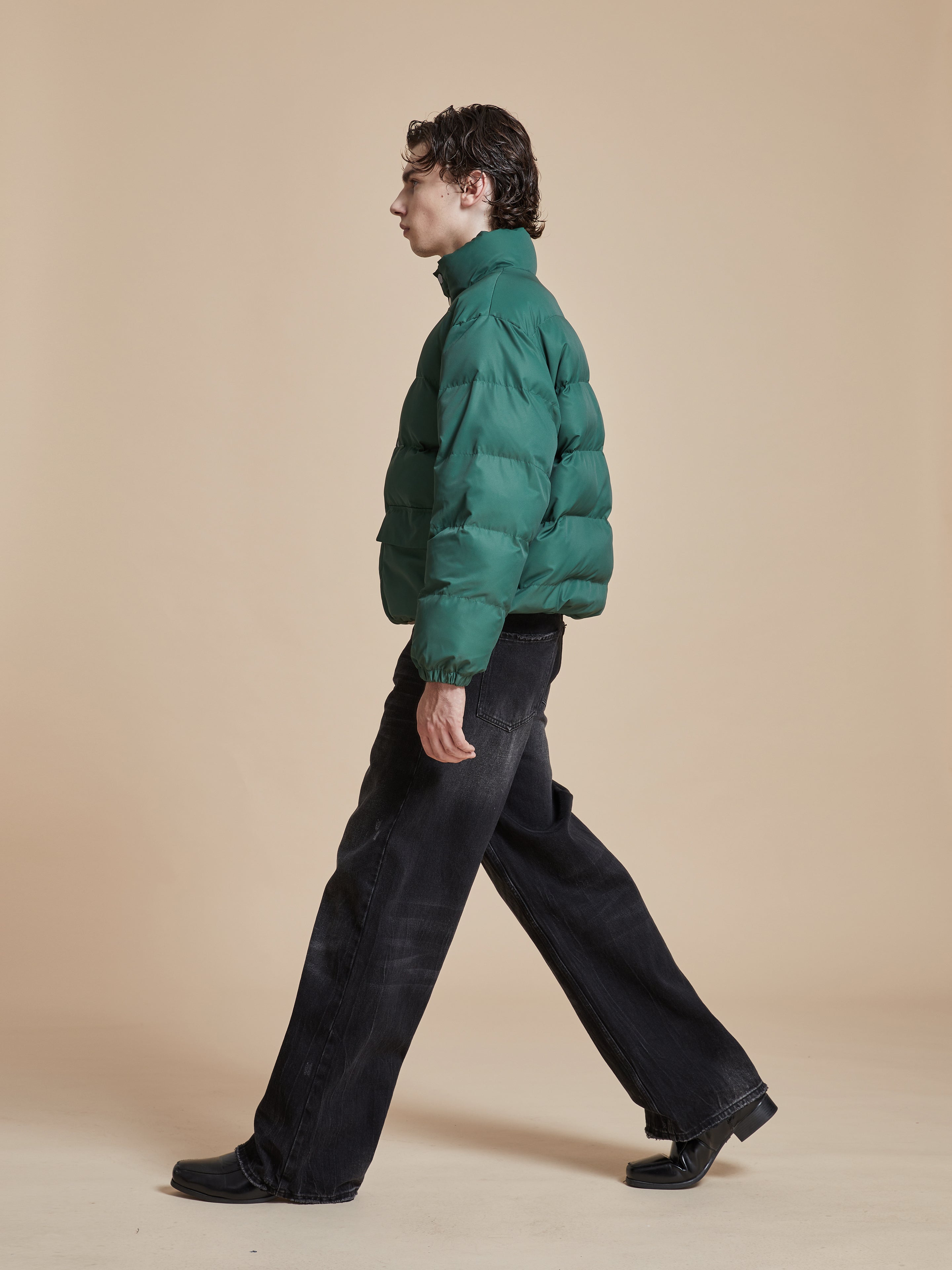 A man in a Laurel Pine Puffer Jacket from Found walking on a beige background.