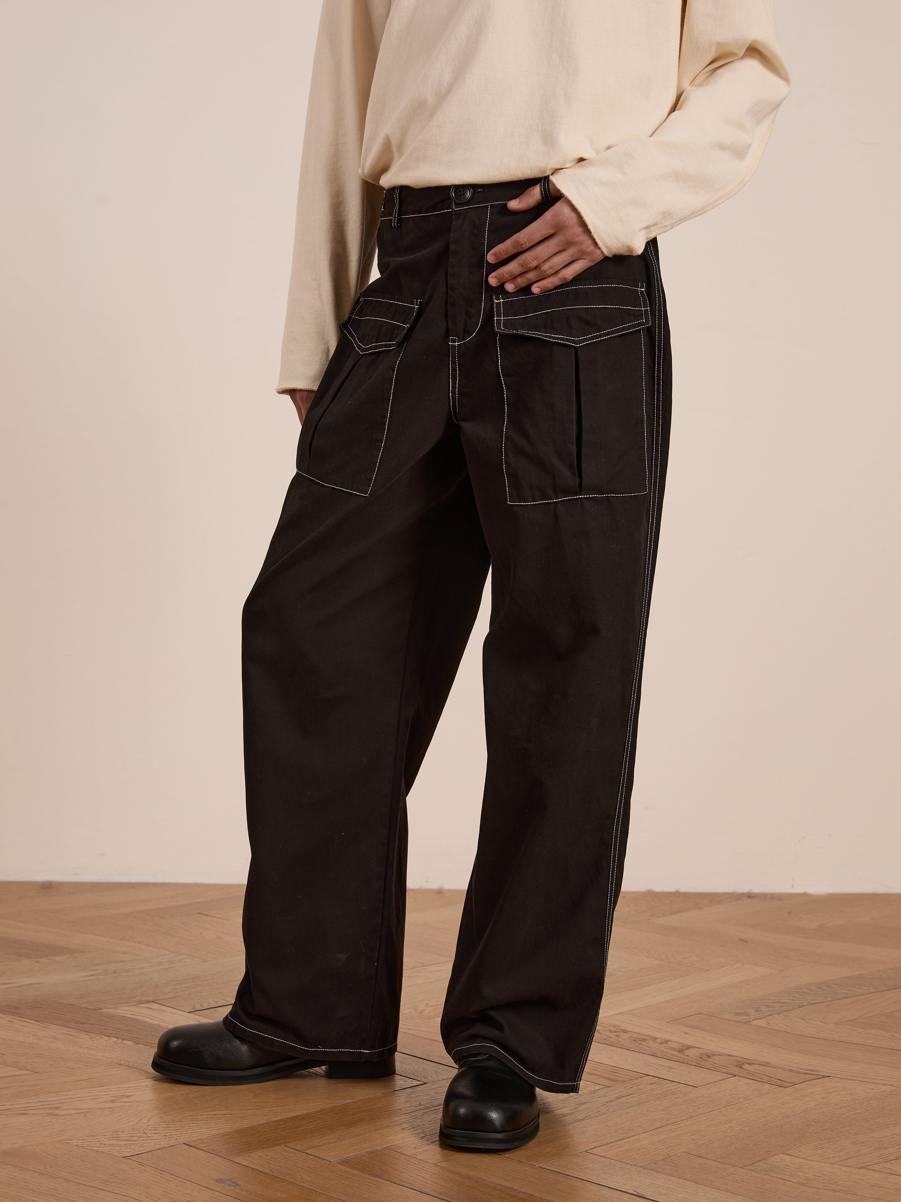 A person in a cream shirt and FOUND's Lucca Black Contrast Pocket Pants, featuring a relaxed straight-leg fit, stands on a wooden floor.