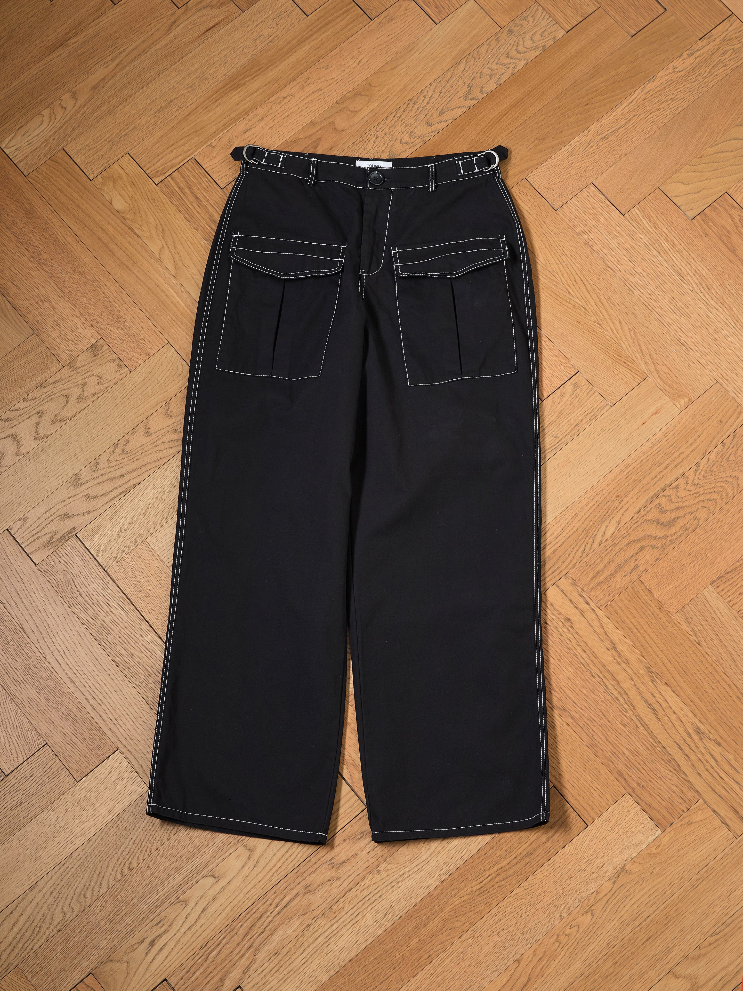 Lucca Black Contrast Pocket Pants by FOUND, featuring white stitching and large front pockets with a relaxed straight-leg fit, are displayed on a wooden herringbone-patterned floor.