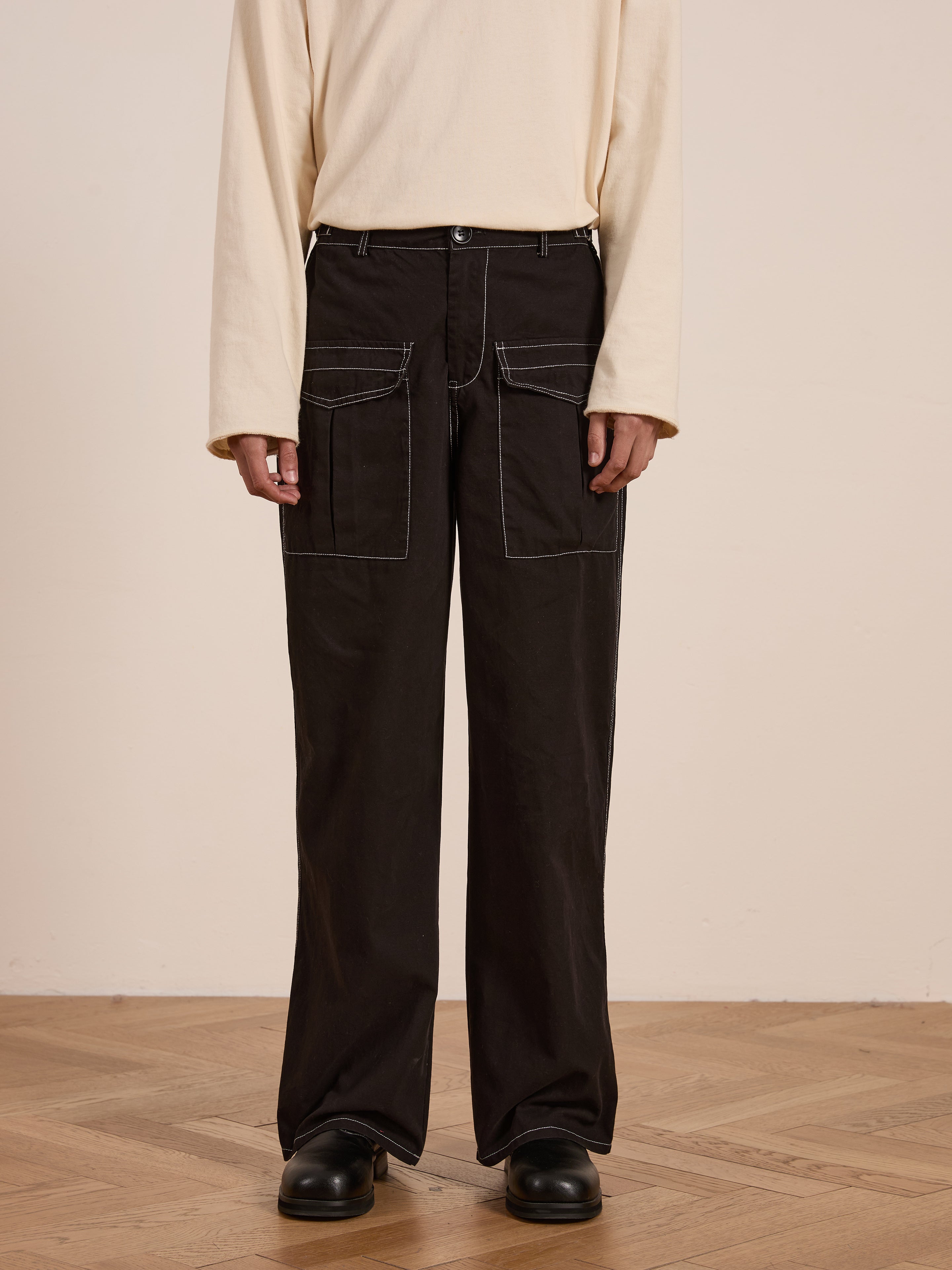 Someone wearing a cream long-sleeve shirt and FOUND's Lucca Black Contrast Pocket Pants with a relaxed straight-leg fit stands on a wooden floor.