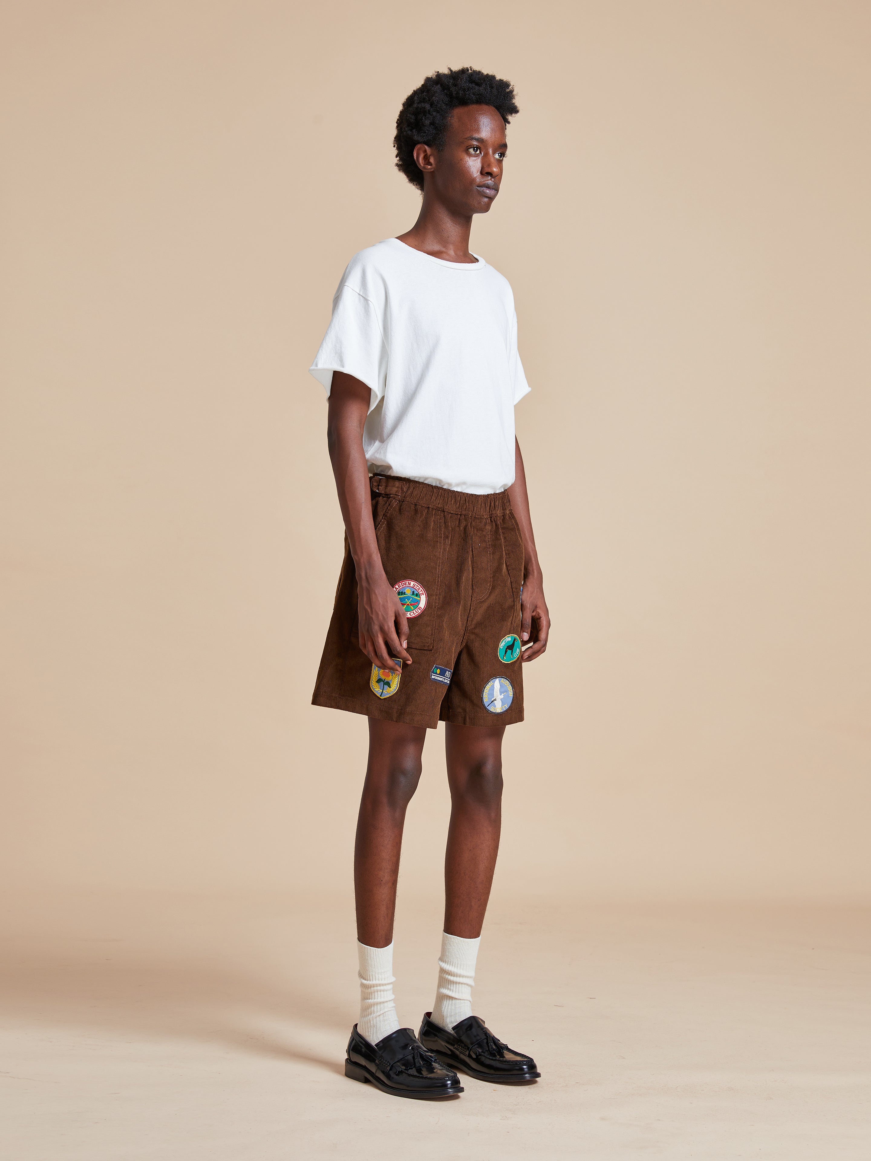 The model is wearing a white t-shirt and Found Canoe Multi Patch Corduroy Shorts.